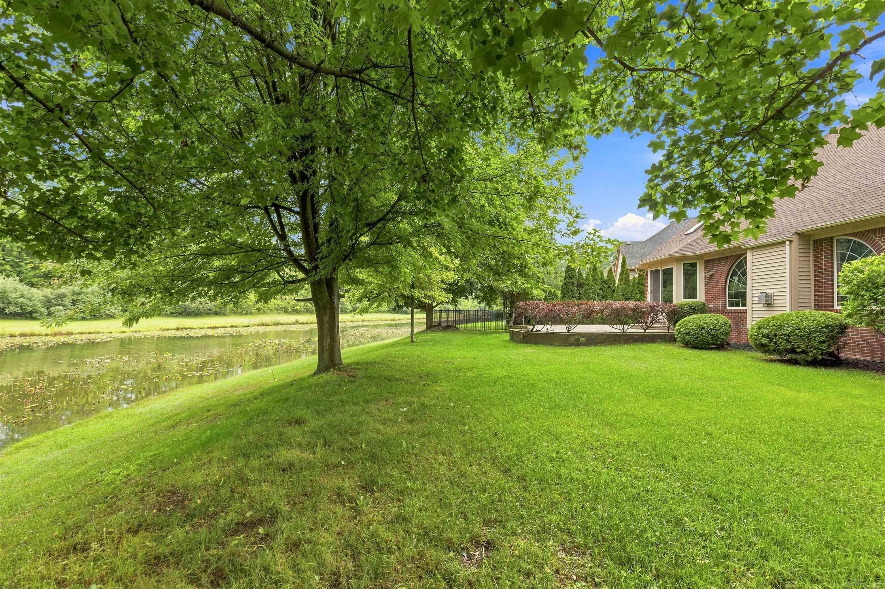 House beside a pond, viewed across a broad lawn shaded by a large tree.