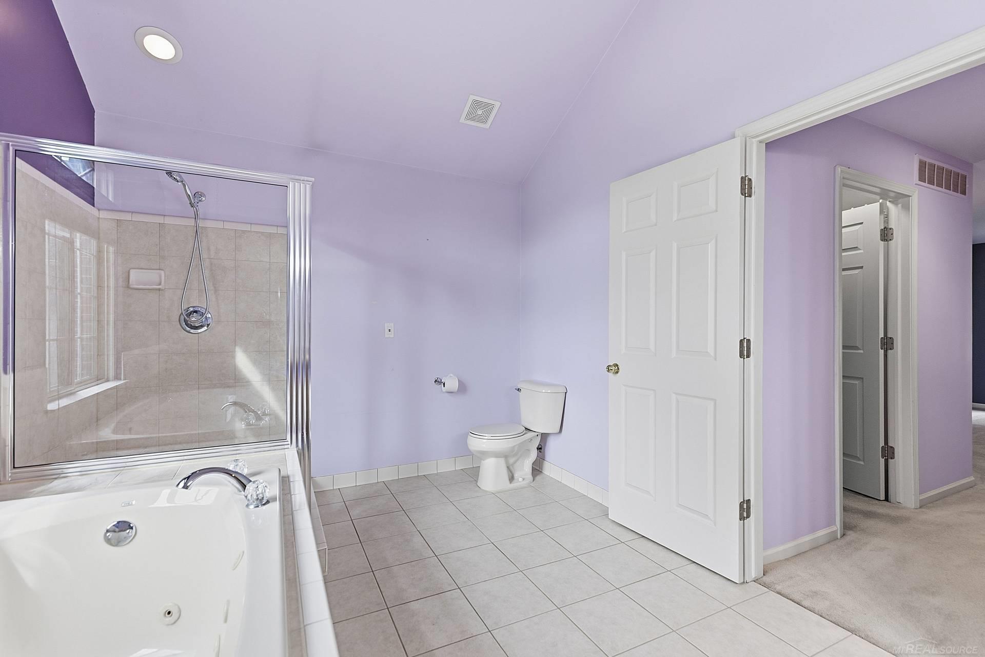 Bathroom with a jetted tub, glass-enclosed shower, toilet, and lavender walls.