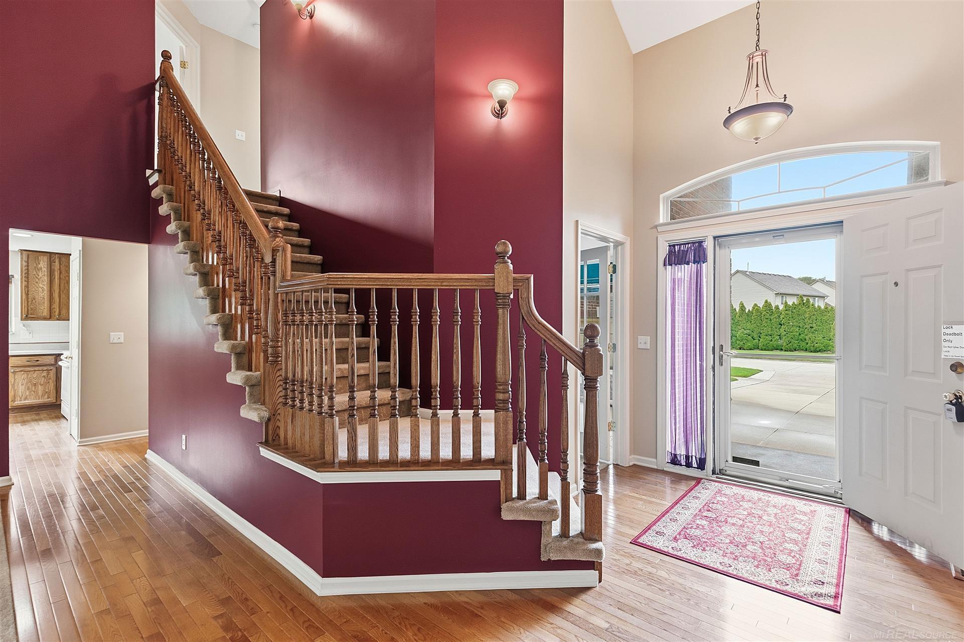 Entry foyer with a carpeted staircase, ornate wood railing, burgundy walls, and an open front door.