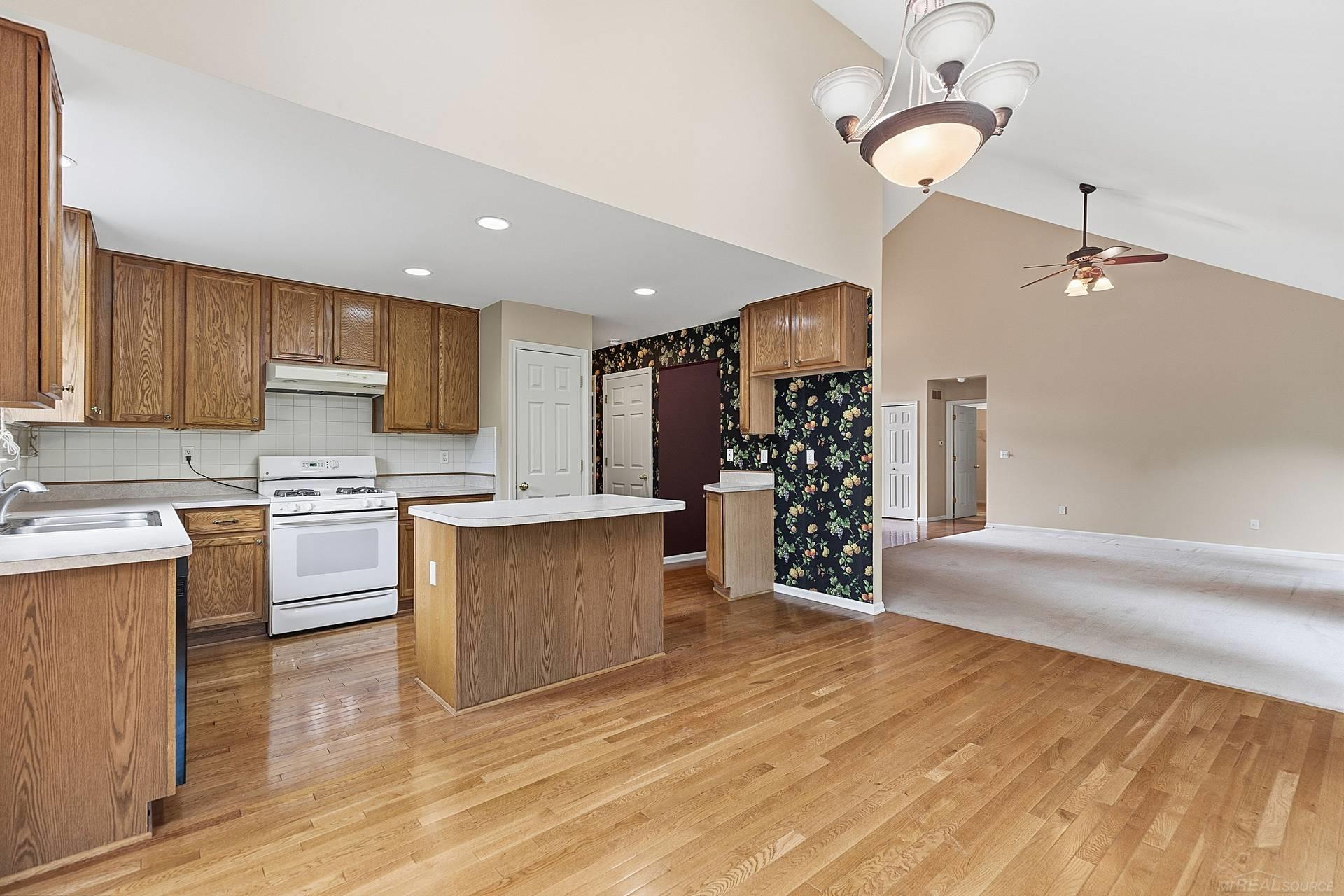 Open kitchen with oak cabinets and island beside a spacious living area with hardwood floors.