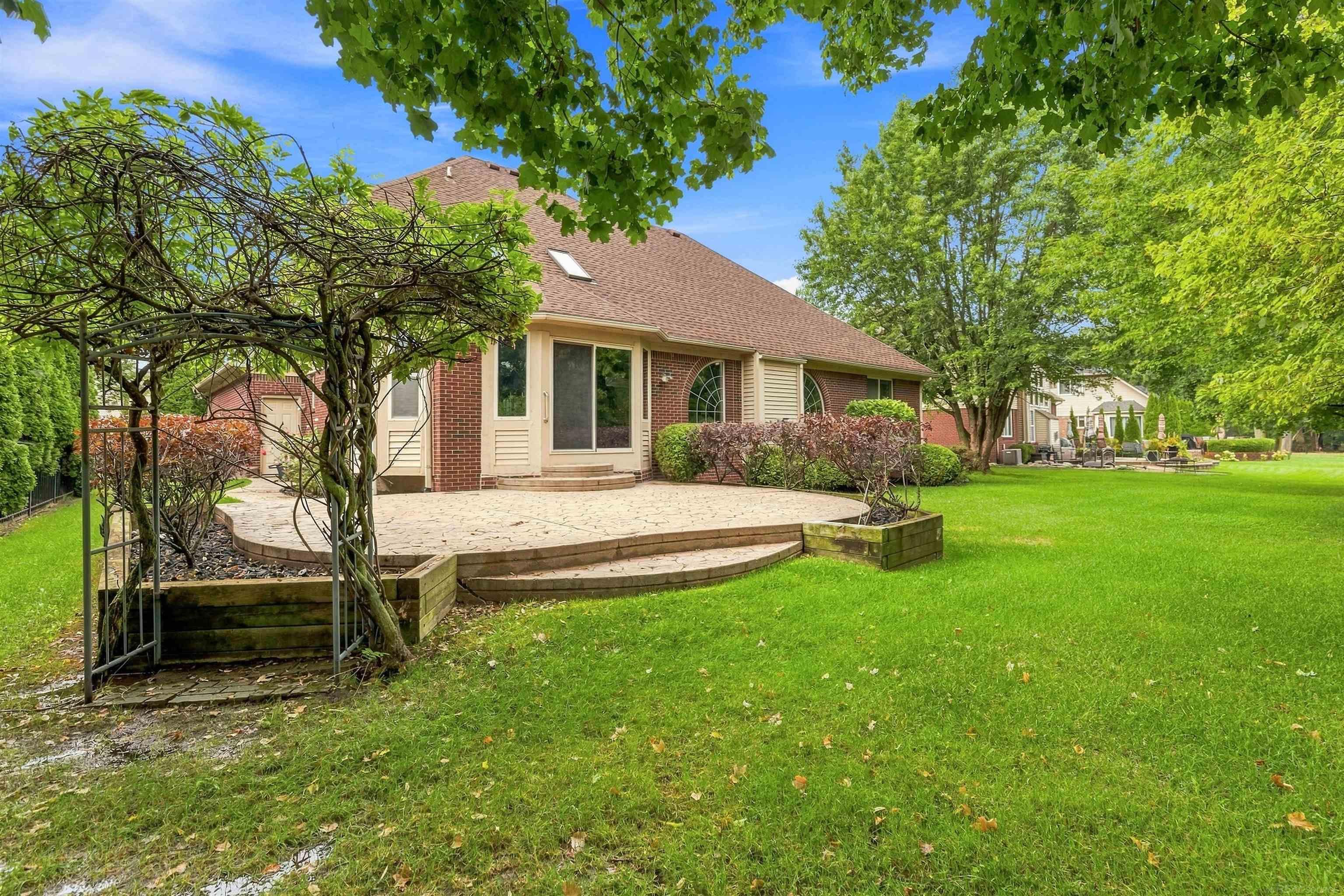 Brick house with a broad patio, vine-covered pergola, and spacious green lawn.
