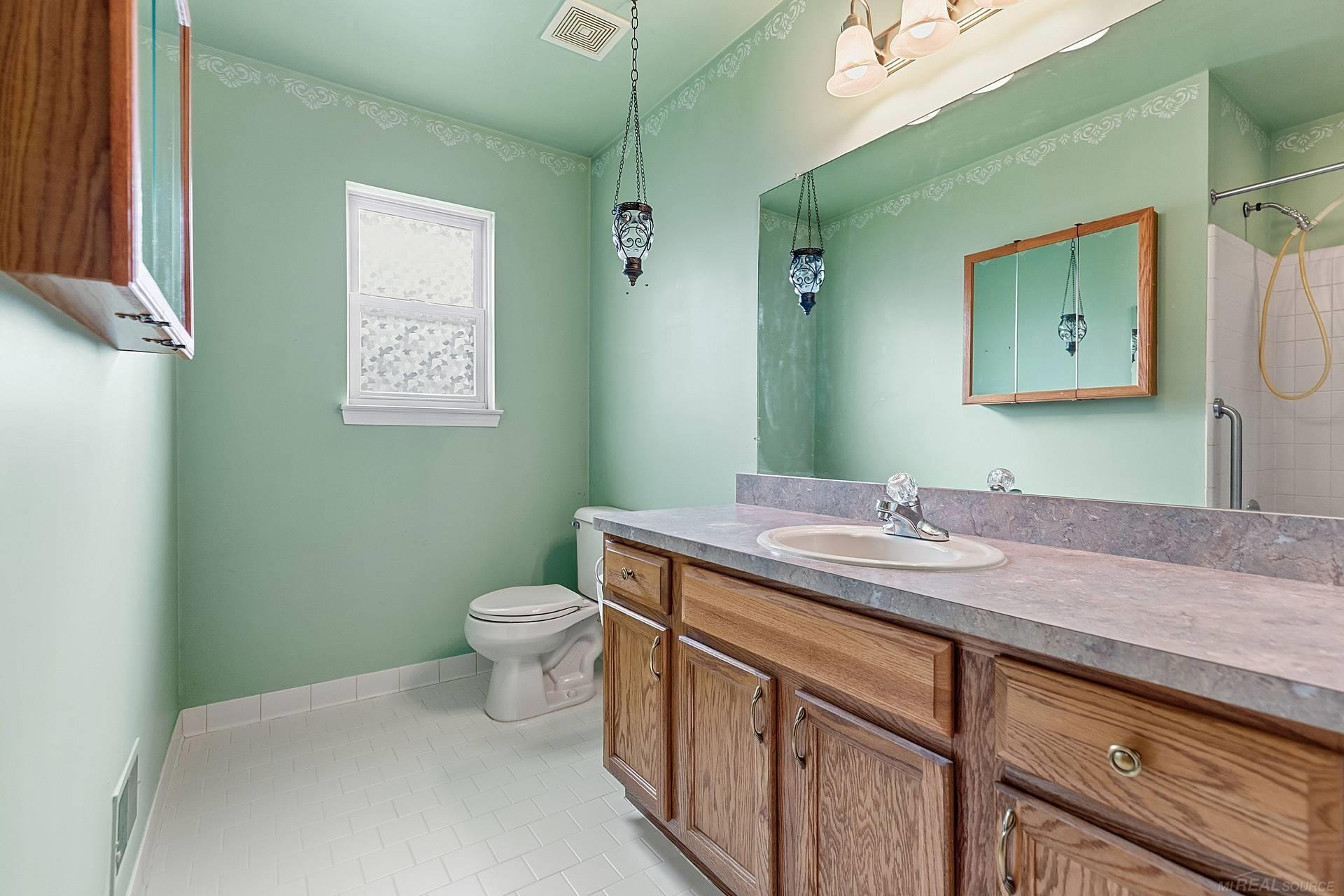 Bathroom with mint-green walls, wood vanity, large mirror, white tile floor, and tiled shower.