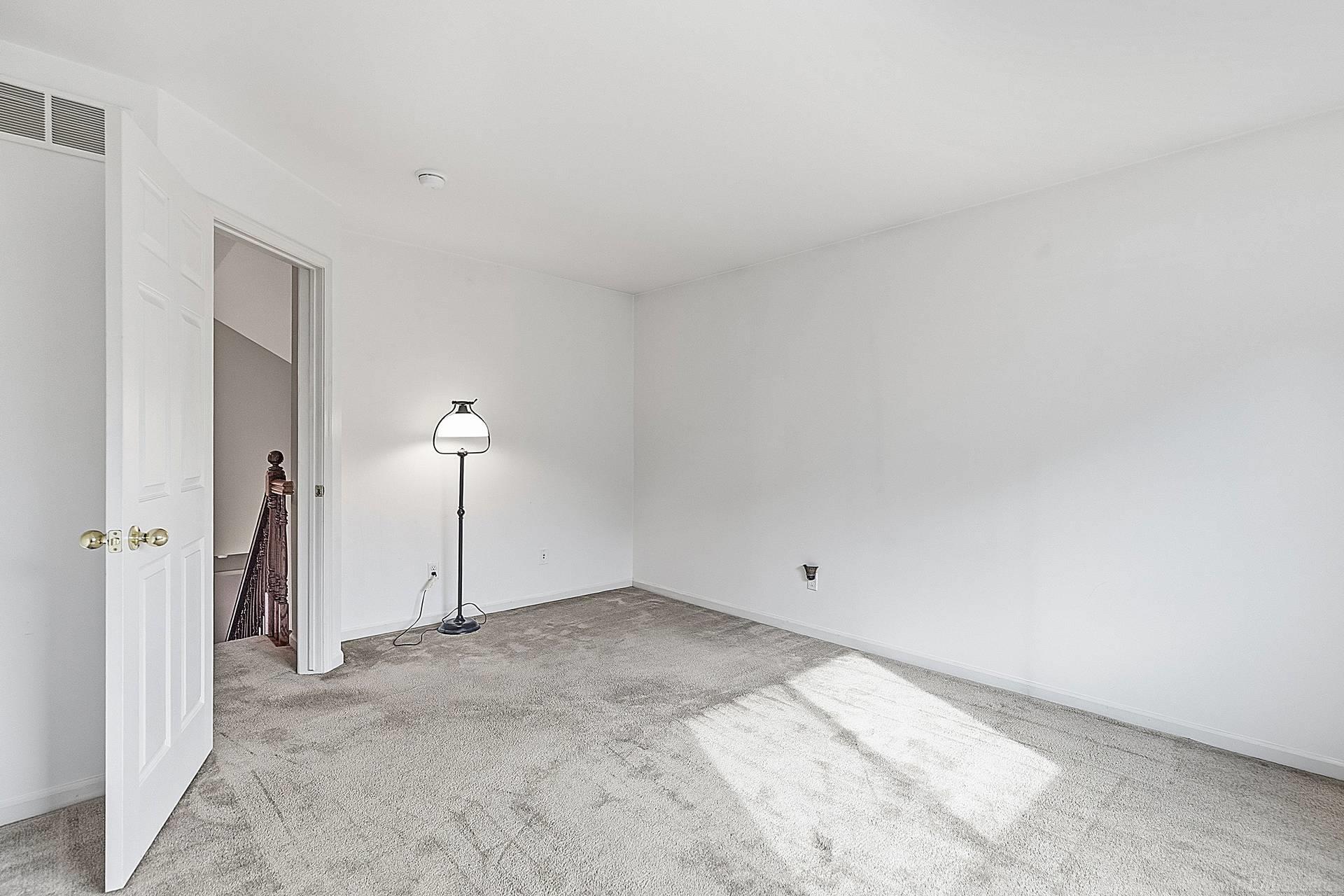 Empty carpeted room with white walls, a floor lamp, and sunlight across the floor.
