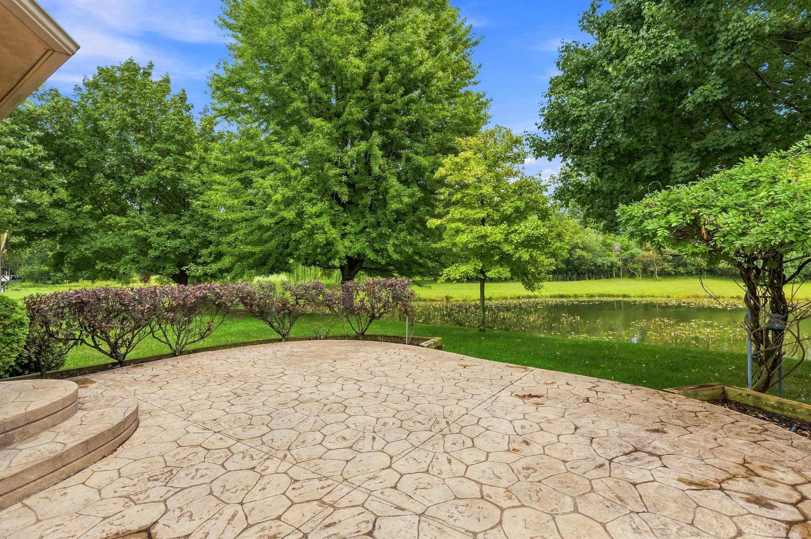 Flagstone patio overlooking a pond, framed by mature trees and greenery.