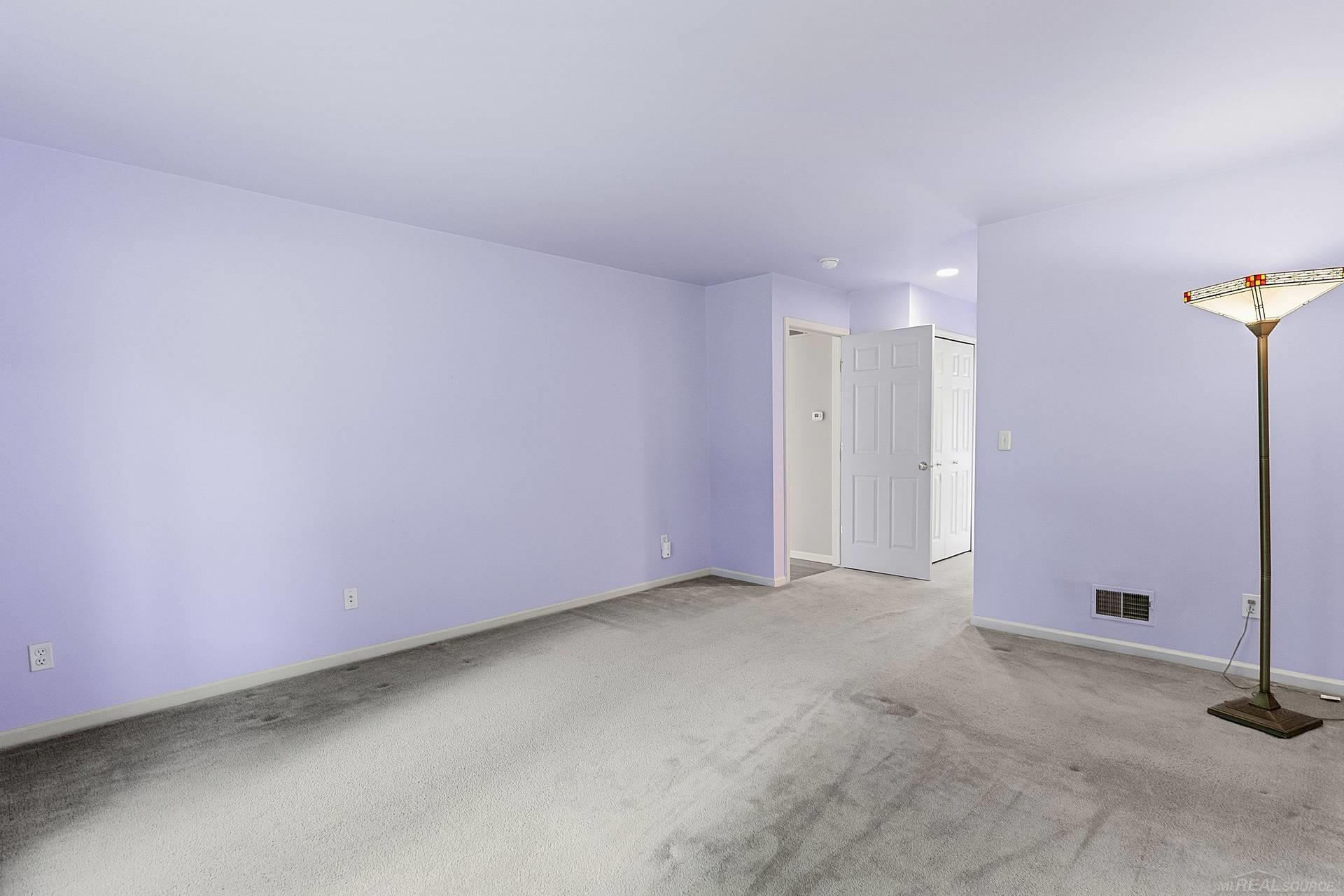 Mostly empty room with lavender walls, gray carpet, an open doorway, and a stained-glass floor lamp.