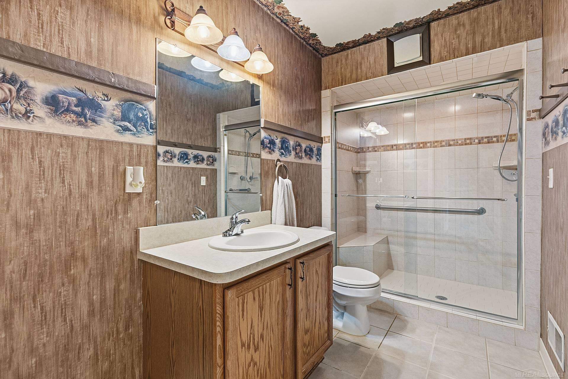 Bathroom with wood vanity and sink beside a tiled walk-in shower with glass doors and grab bars.