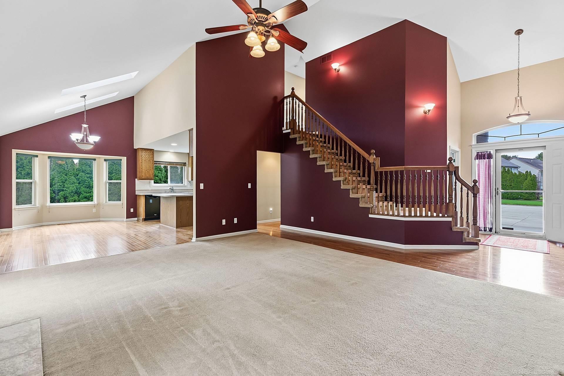 Open living room with vaulted ceilings, burgundy walls, and a prominent wooden staircase.