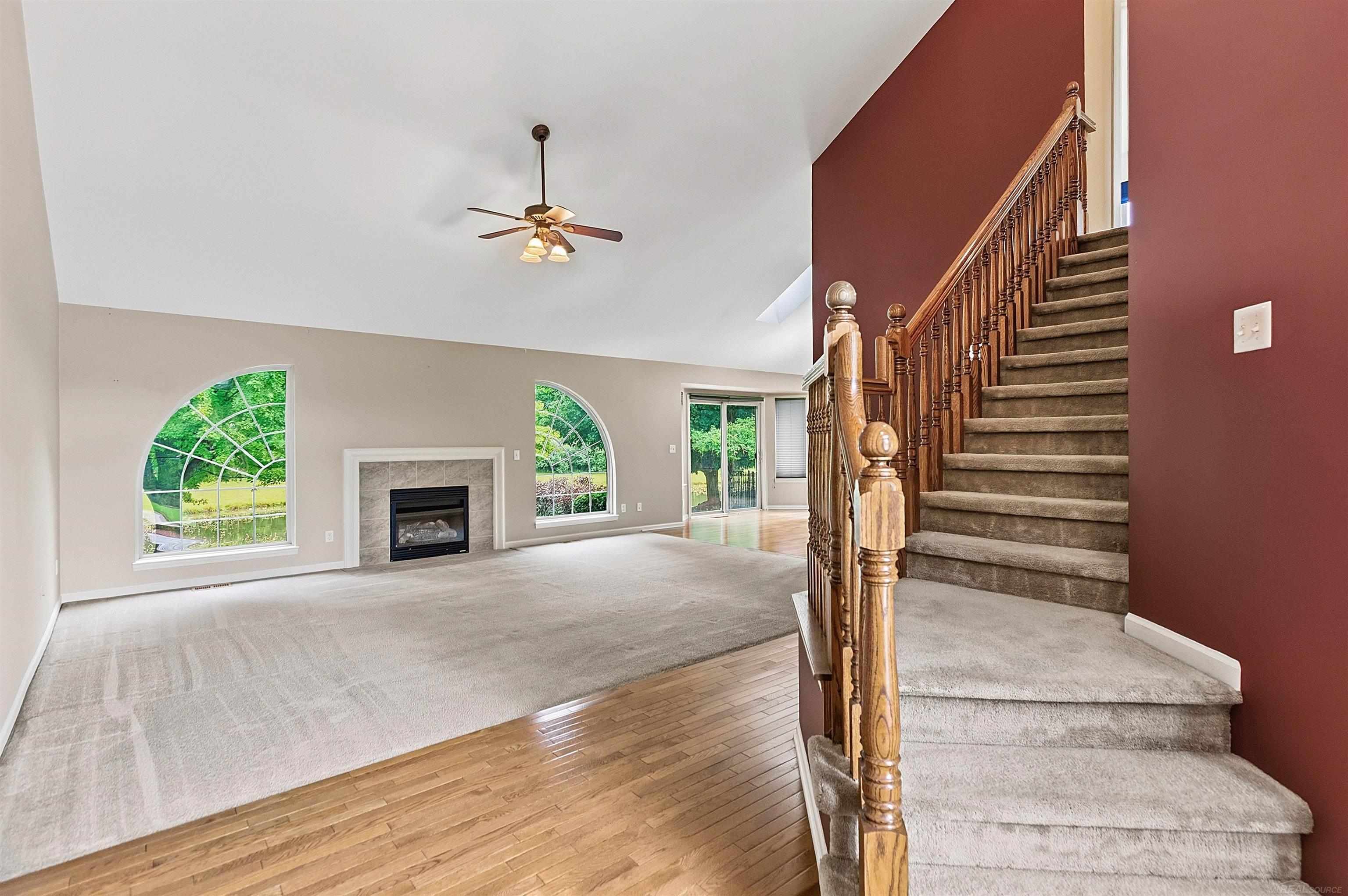 Living room with a carpeted staircase, fireplace, and two large arched windows.