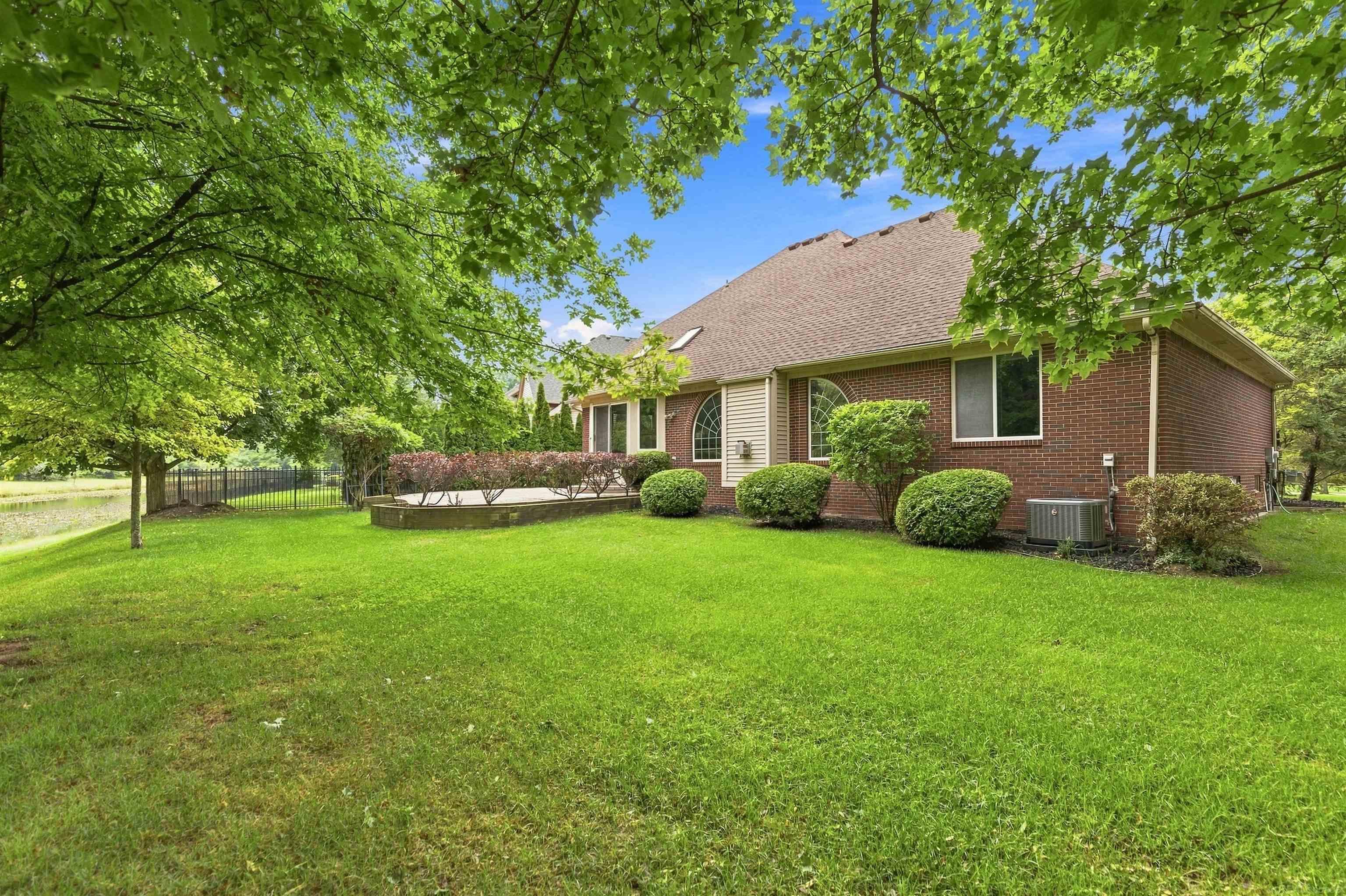 Brick home beside a leafy lawn, with a raised patio and pond along the fenced yard.