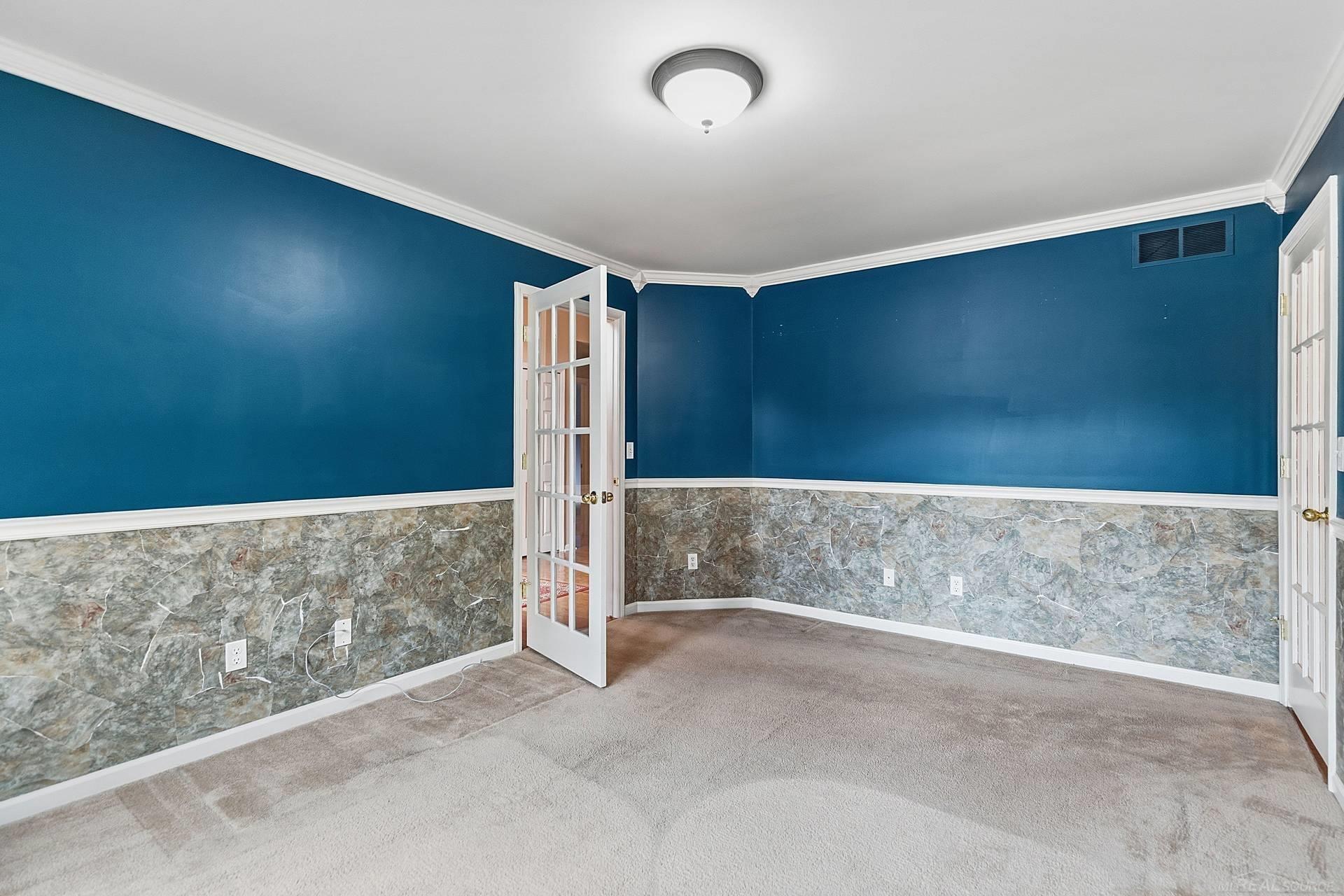 Empty room with blue walls, marble-patterned wainscoting, beige carpet, and open French doors.