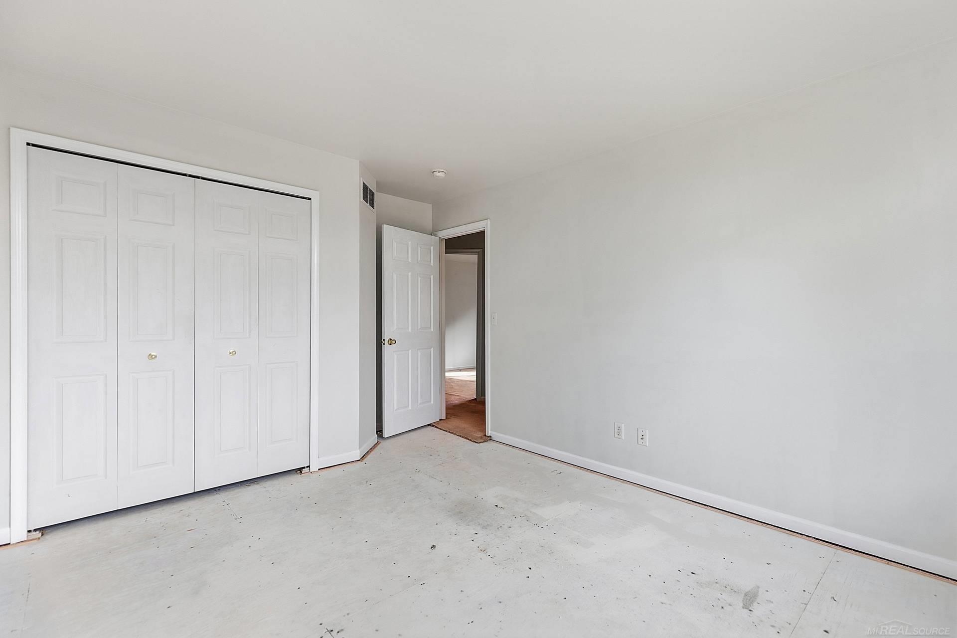 Empty bedroom with white folding closet doors, a bare floor, and an open doorway.