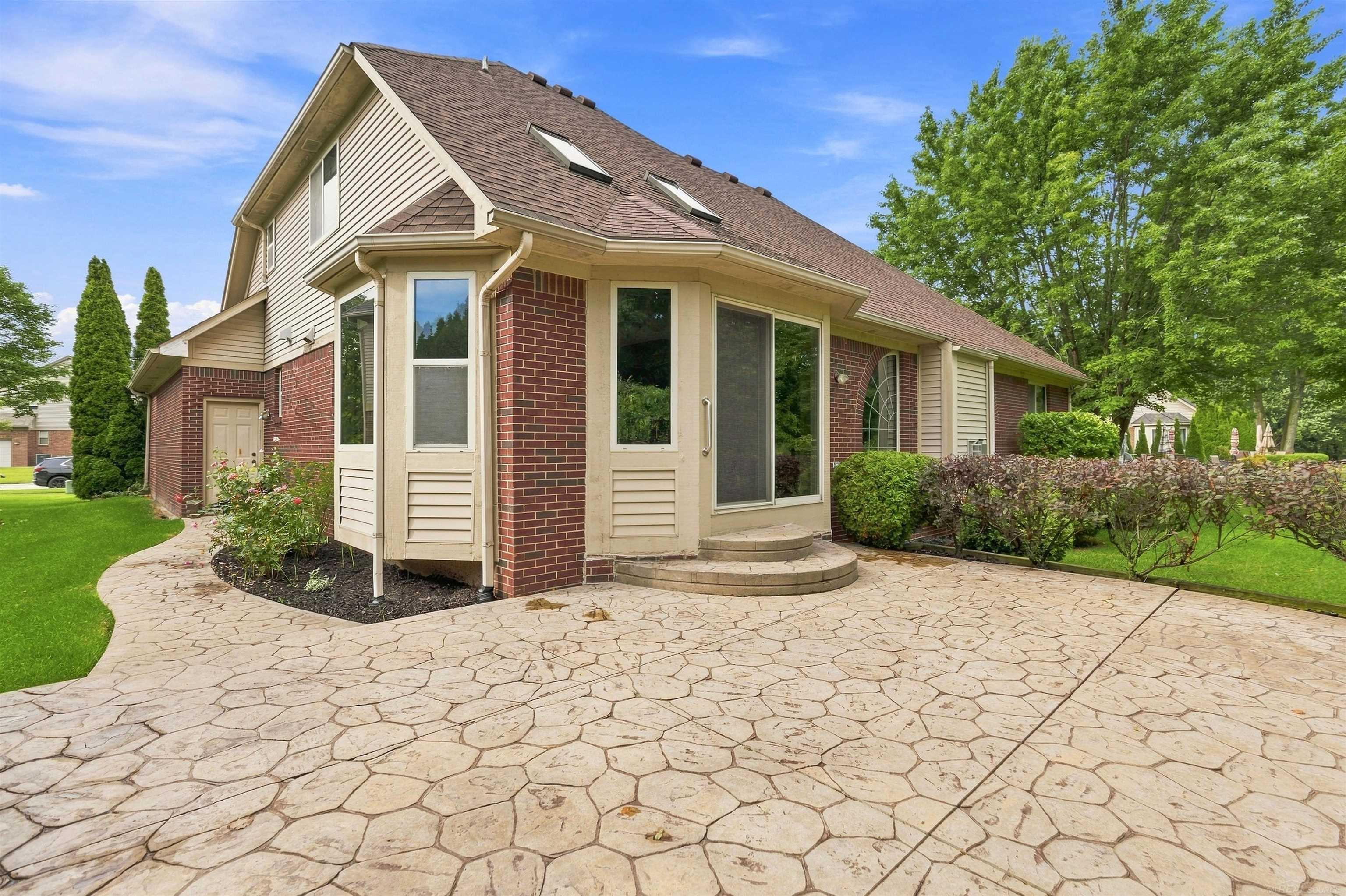 Two-story brick and beige-sided house beside a broad stamped-stone patio and landscaped yard.