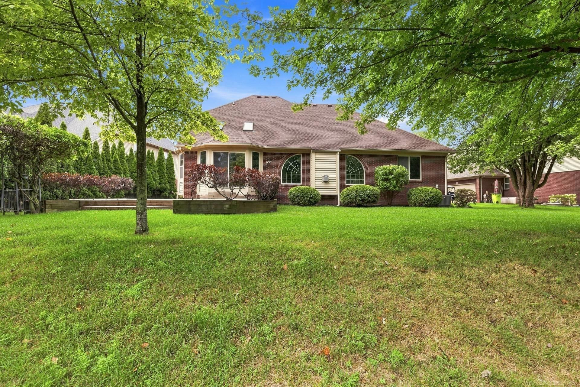 Rear of a brick house with arched windows, landscaped shrubs, and a broad lawn beneath leafy trees.