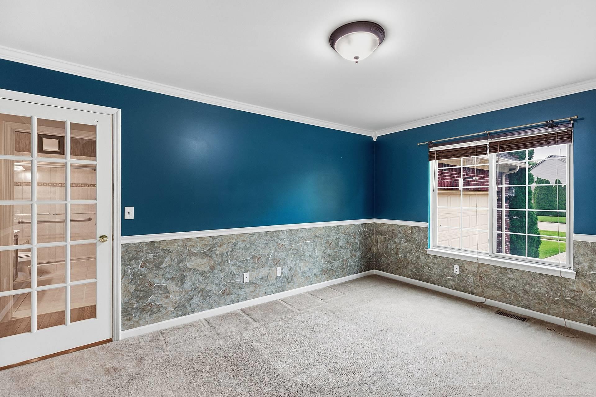 Empty carpeted room with blue walls, stone-patterned wainscoting, and a large window.