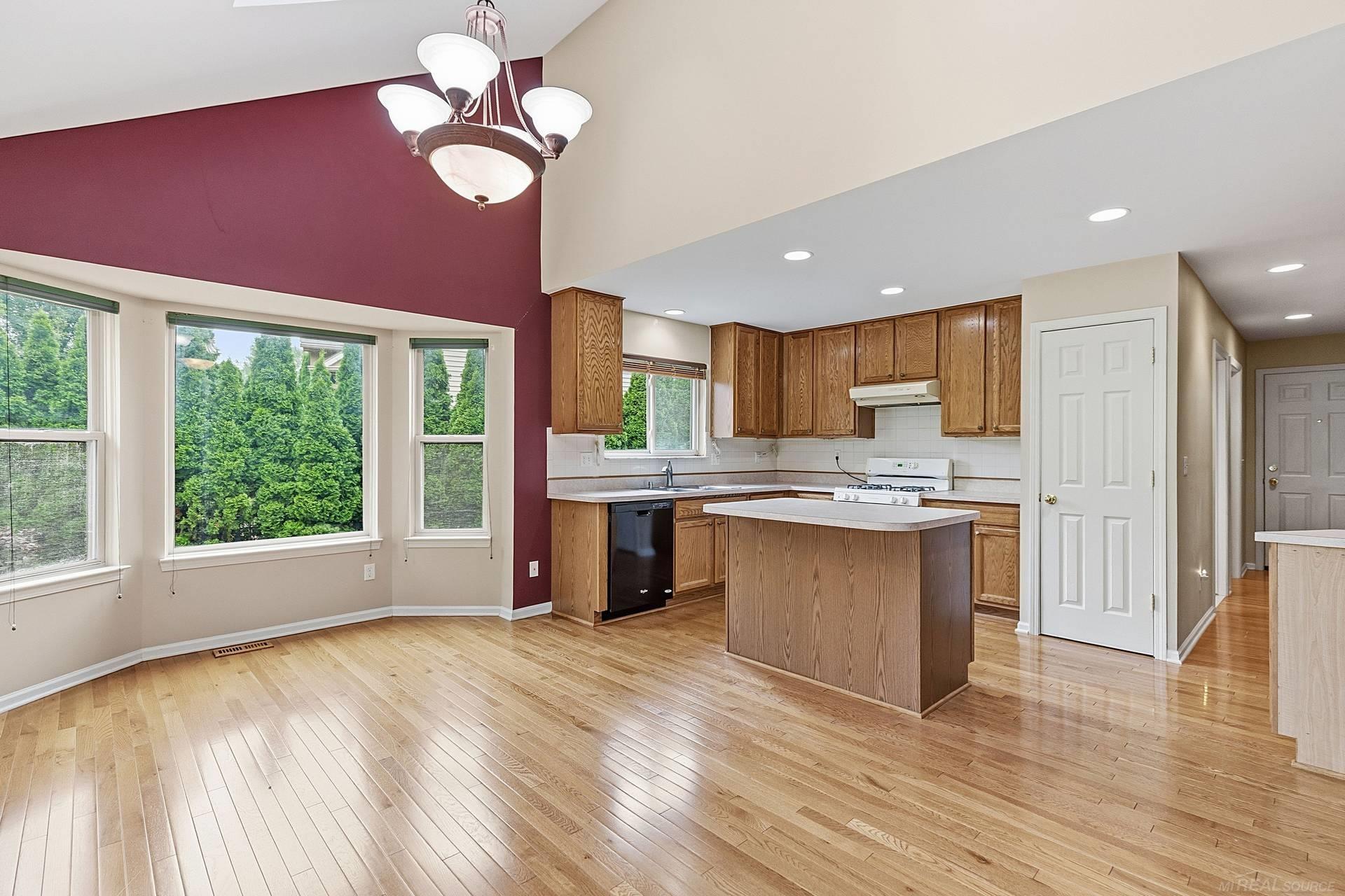 Open kitchen with oak cabinetry, central island, hardwood floors, and a burgundy accent wall.