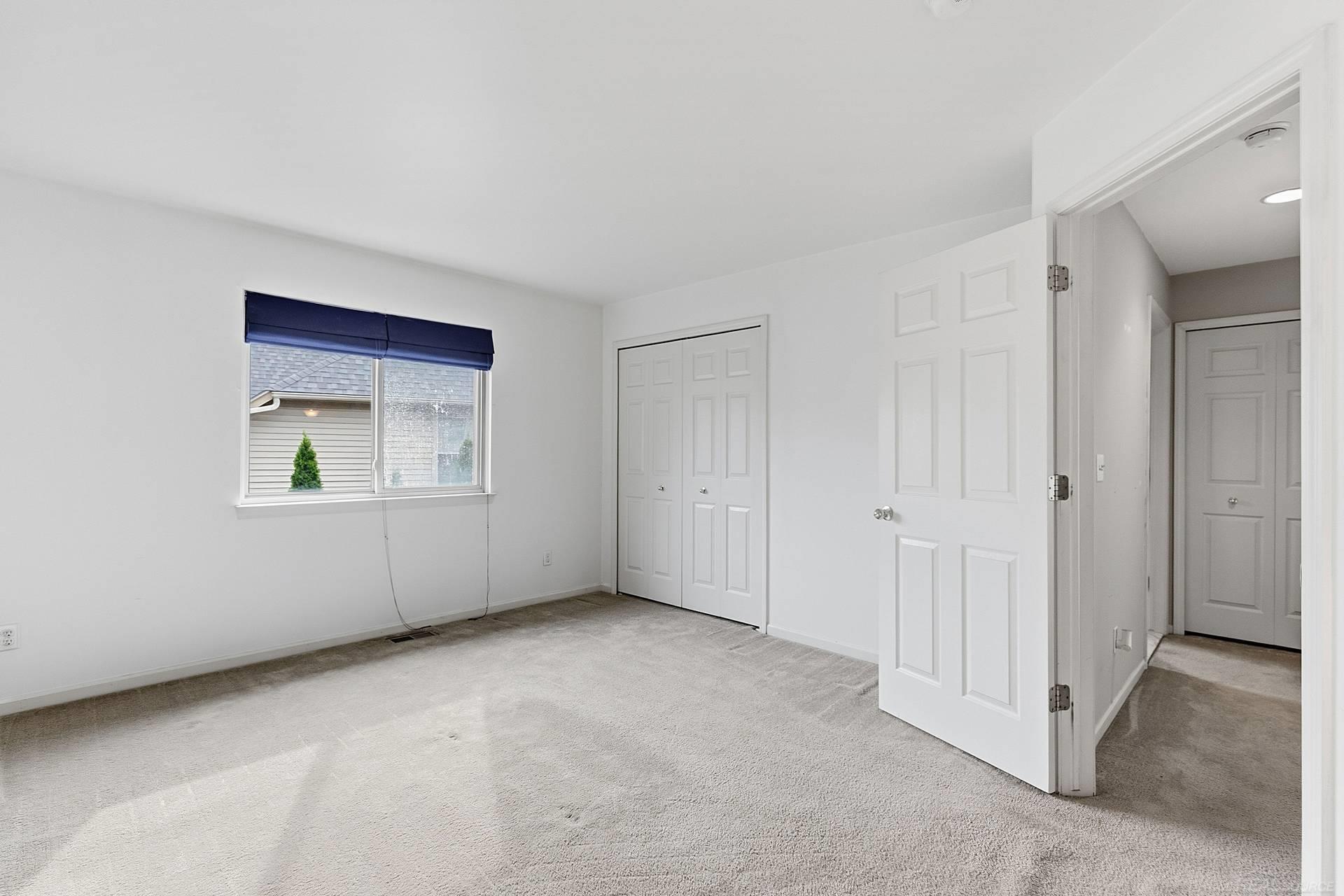 Empty carpeted bedroom with a window, double-door closet, and open doorway to the hall.
