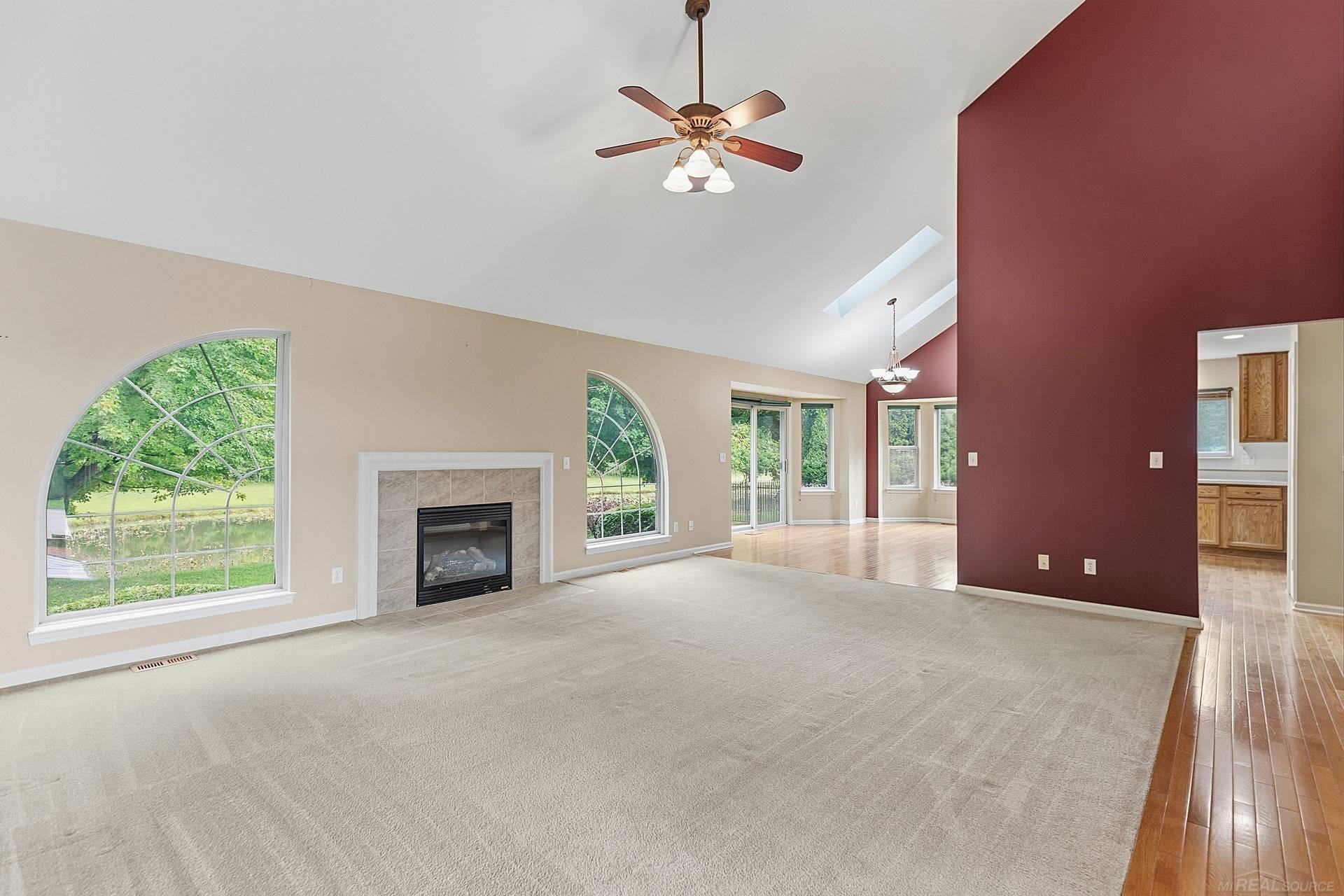 Empty living room with a gas fireplace, vaulted ceiling, and large arched windows.