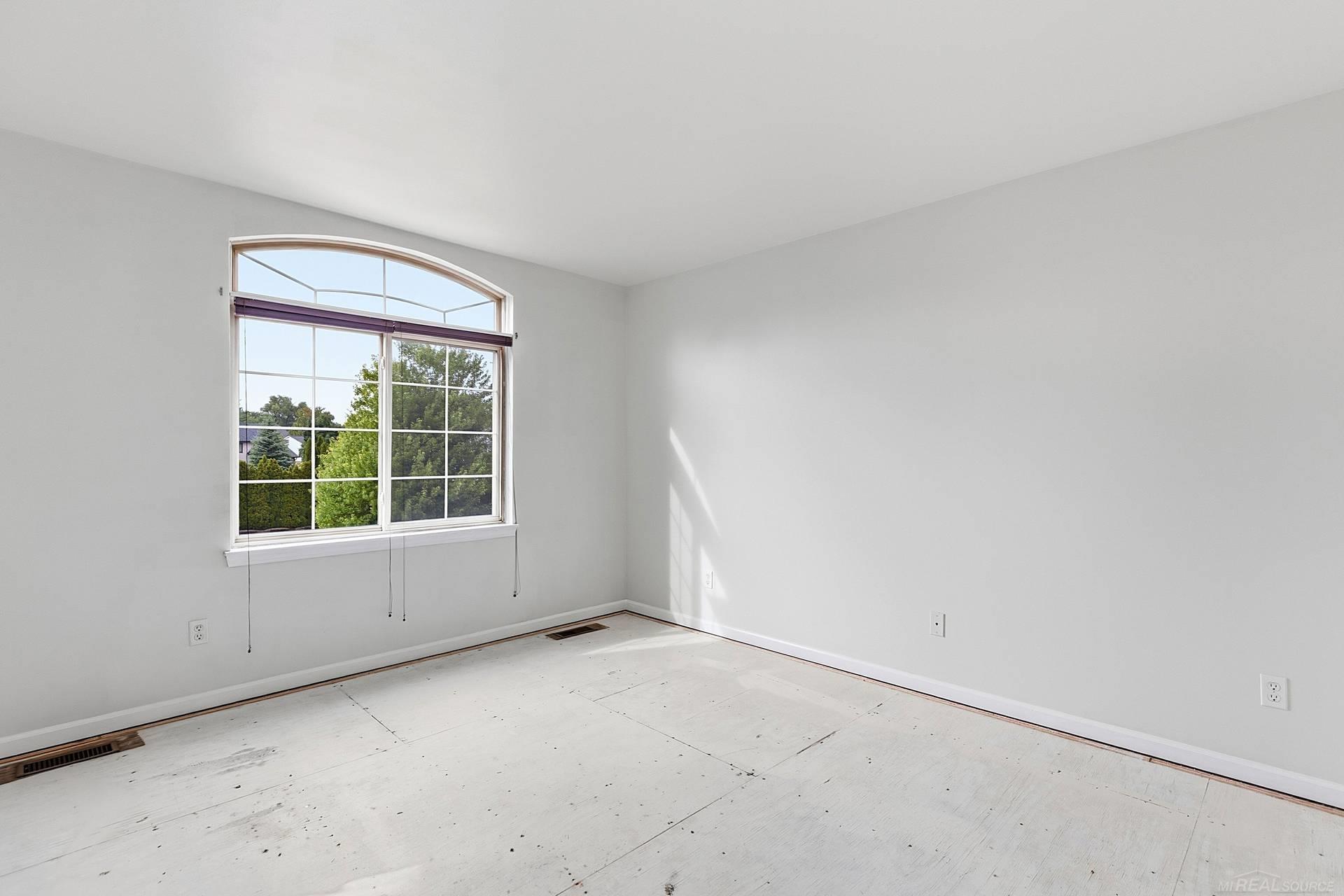 Empty room with a large arched window and sunlight across its bare floor.