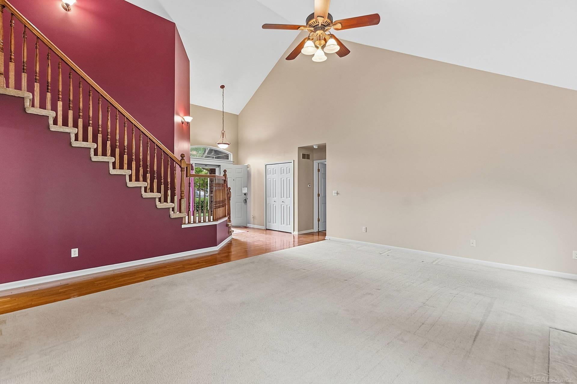 Vacant living room with a vaulted ceiling, burgundy stair wall, and hardwood flooring near the entry.