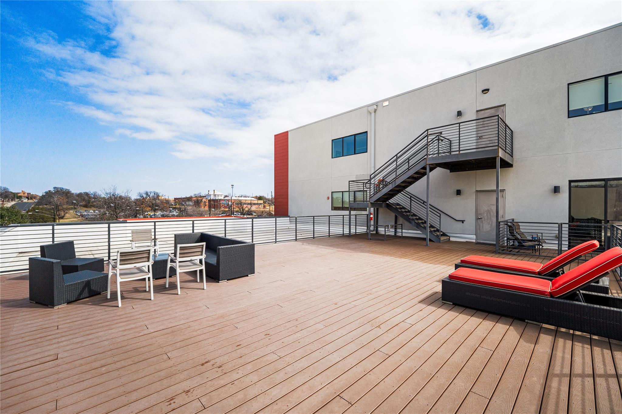 Rooftop deck with wood-plank flooring, outdoor seating, red-cushioned loungers, and exterior stairs.
