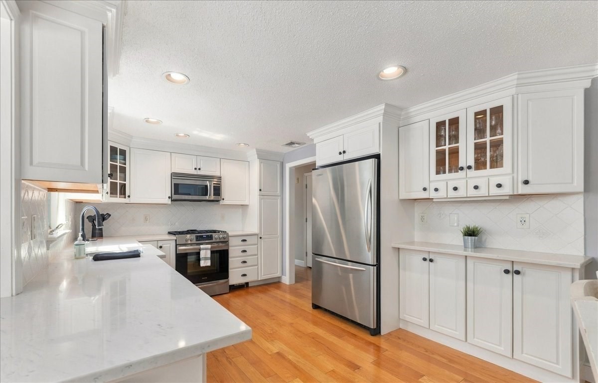 Bright white kitchen with stainless steel appliances, stone counters, and warm hardwood floors.