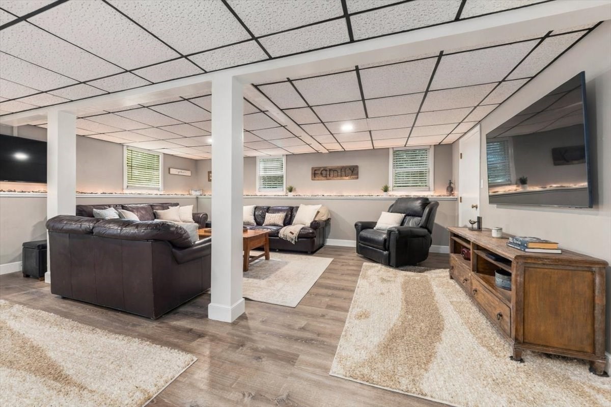 Basement family room with leather seating, a wall-mounted TV, and wood-look floors.