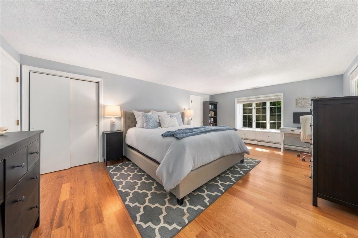Bedroom with a king-size bed, patterned rug, hardwood floors, and a desk beside the window.