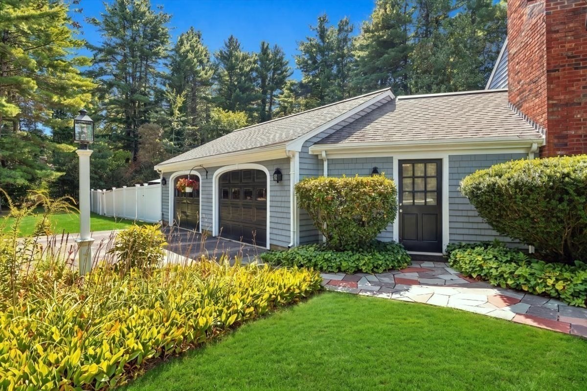 Gray-shingled garage wing with two doors and a side entrance, surrounded by a garden and lawn.