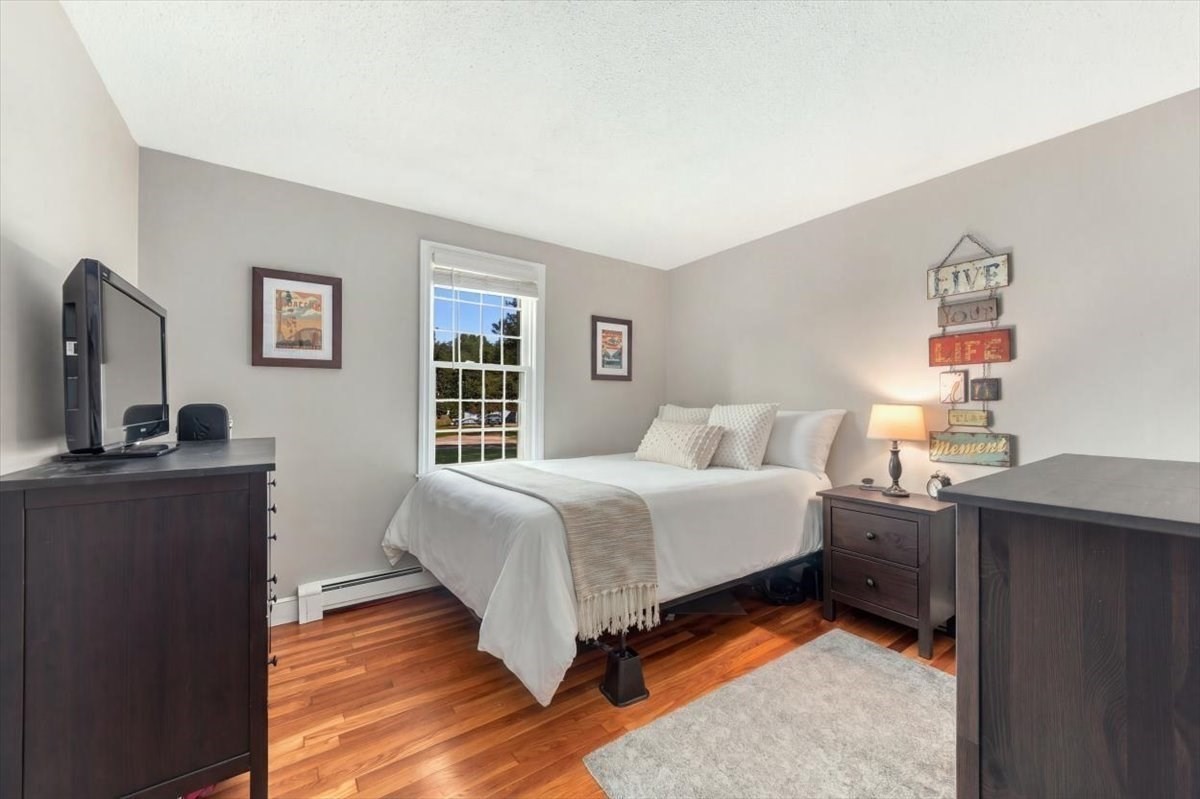 Bedroom with a white bed, dark wood furniture, hardwood floors, and a window overlooking the street.