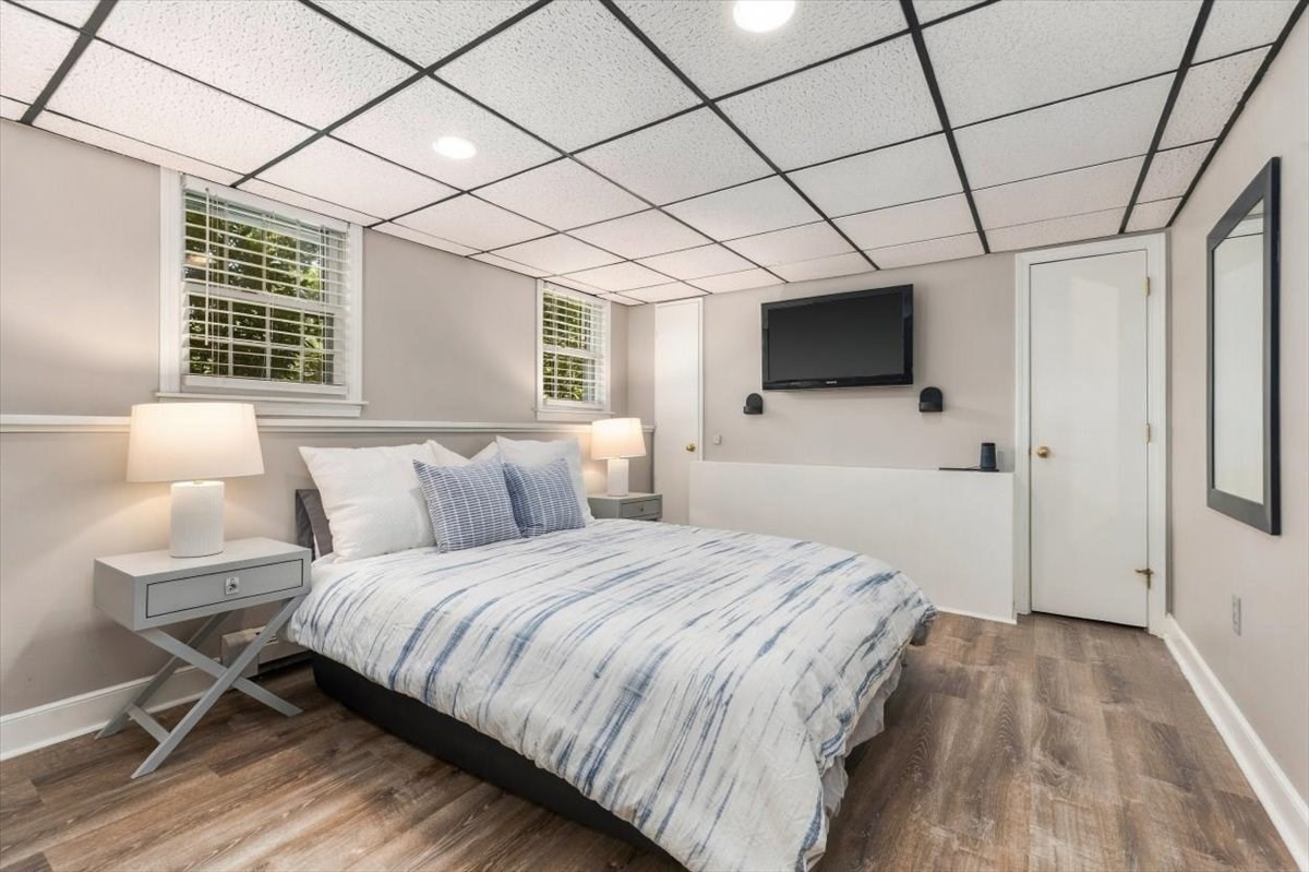 Staged bedroom with blue-and-white bedding, two windows, and a wall-mounted television.