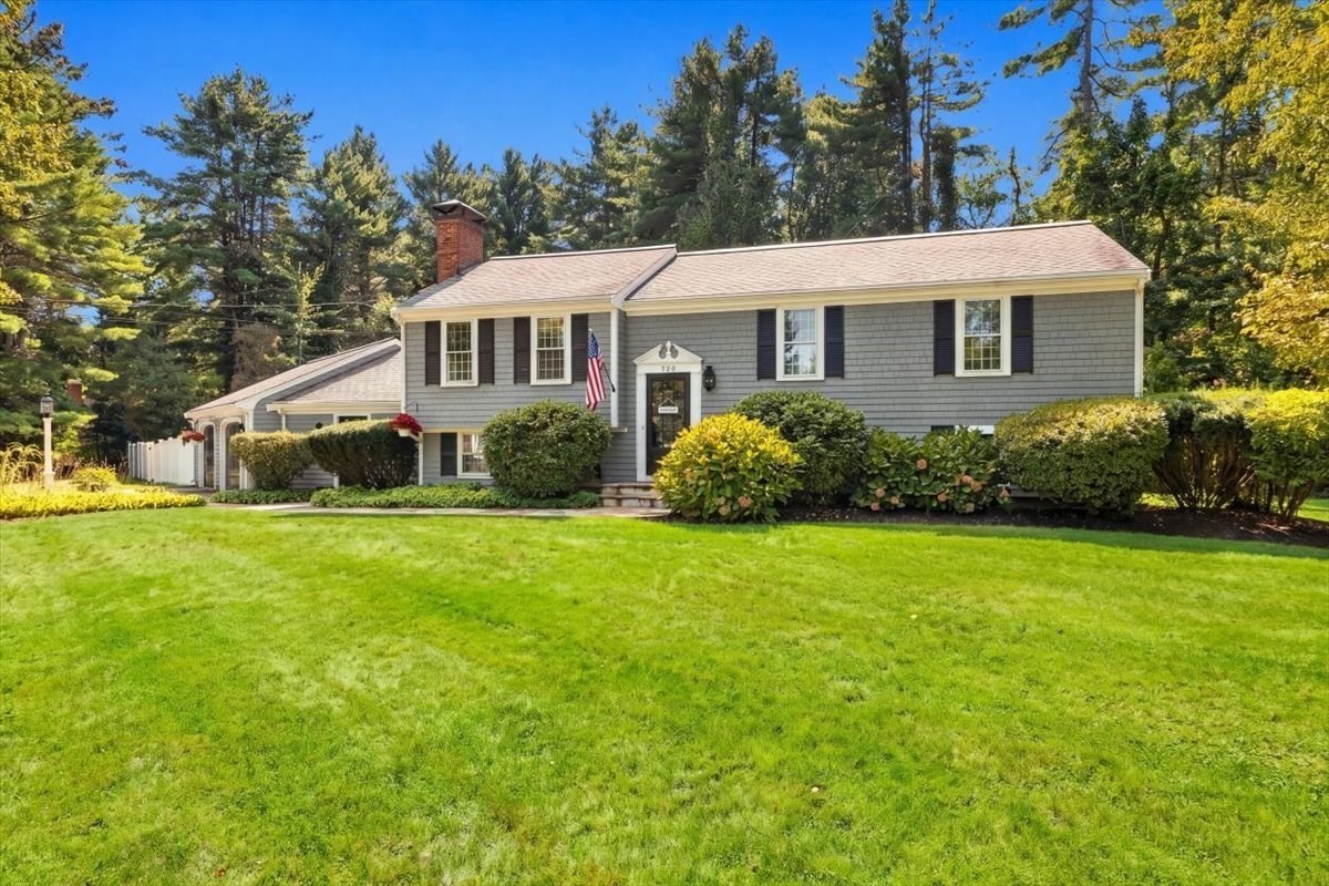 Gray split-level house with black shutters, a brick chimney, and a wide green lawn.