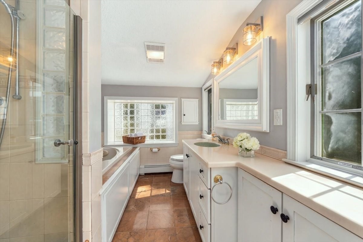 Bathroom with glass-enclosed shower, built-in tub, long white vanity, and glass-block window.