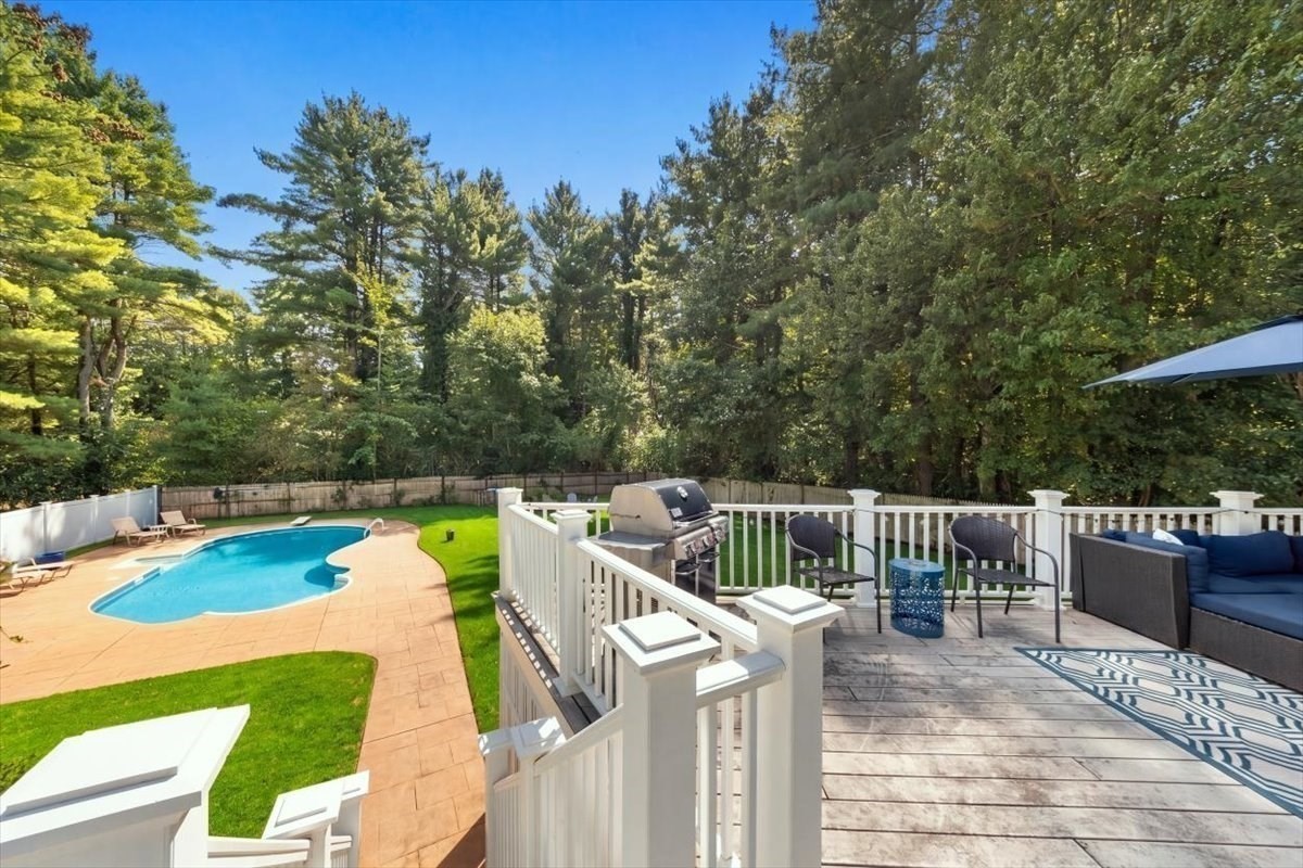 Backyard pool and paved patio beside a raised deck furnished with seating and a grill.