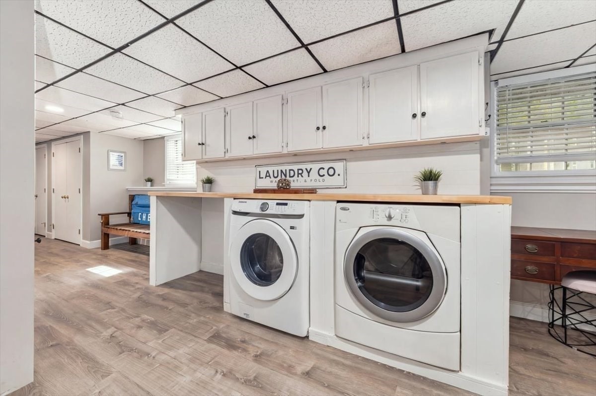 Laundry room with front-loading washer and dryer, white cabinetry, and a long wood countertop.