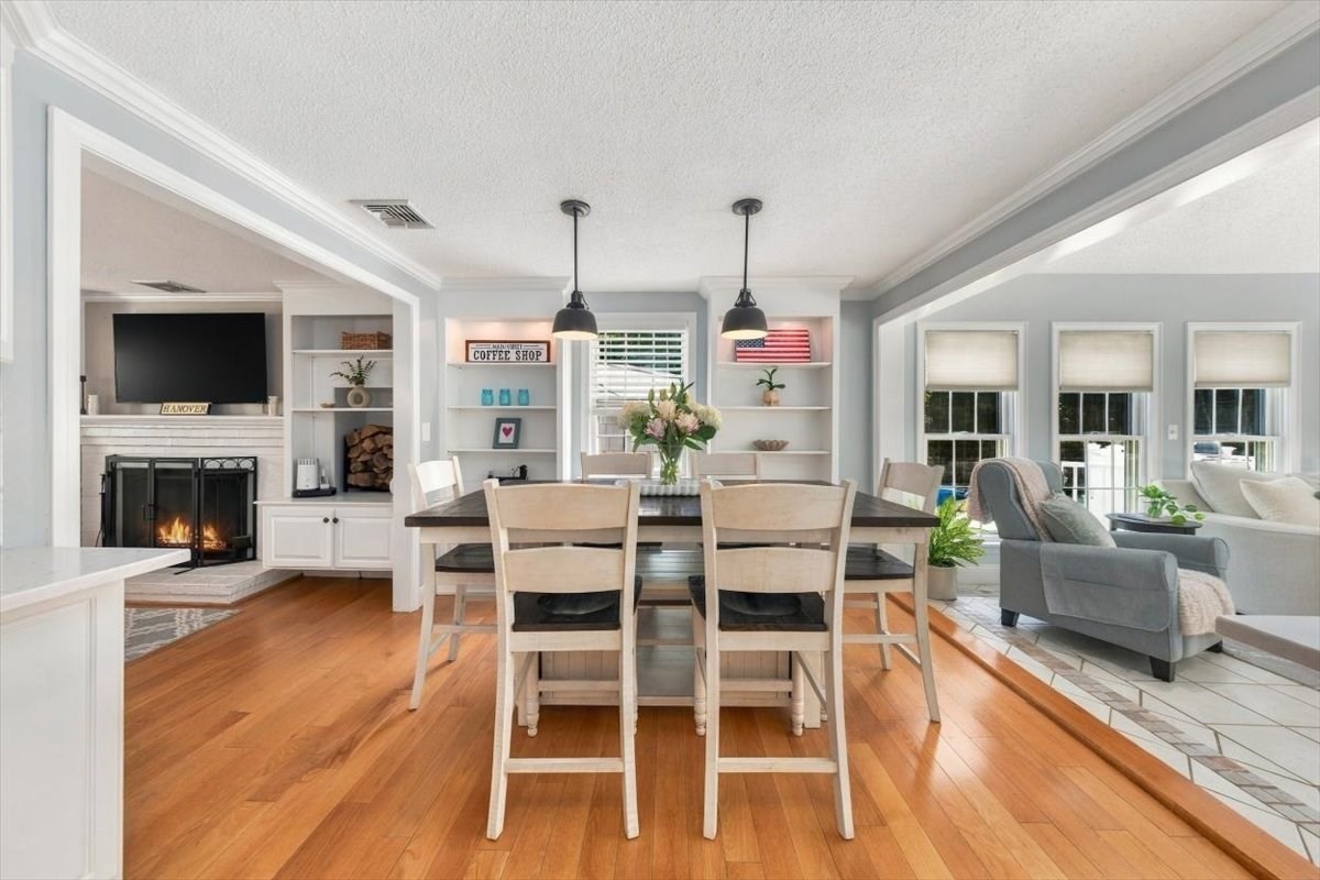 Dining area with a wooden table, built-in shelves, and an adjoining living room with a lit fireplace.
