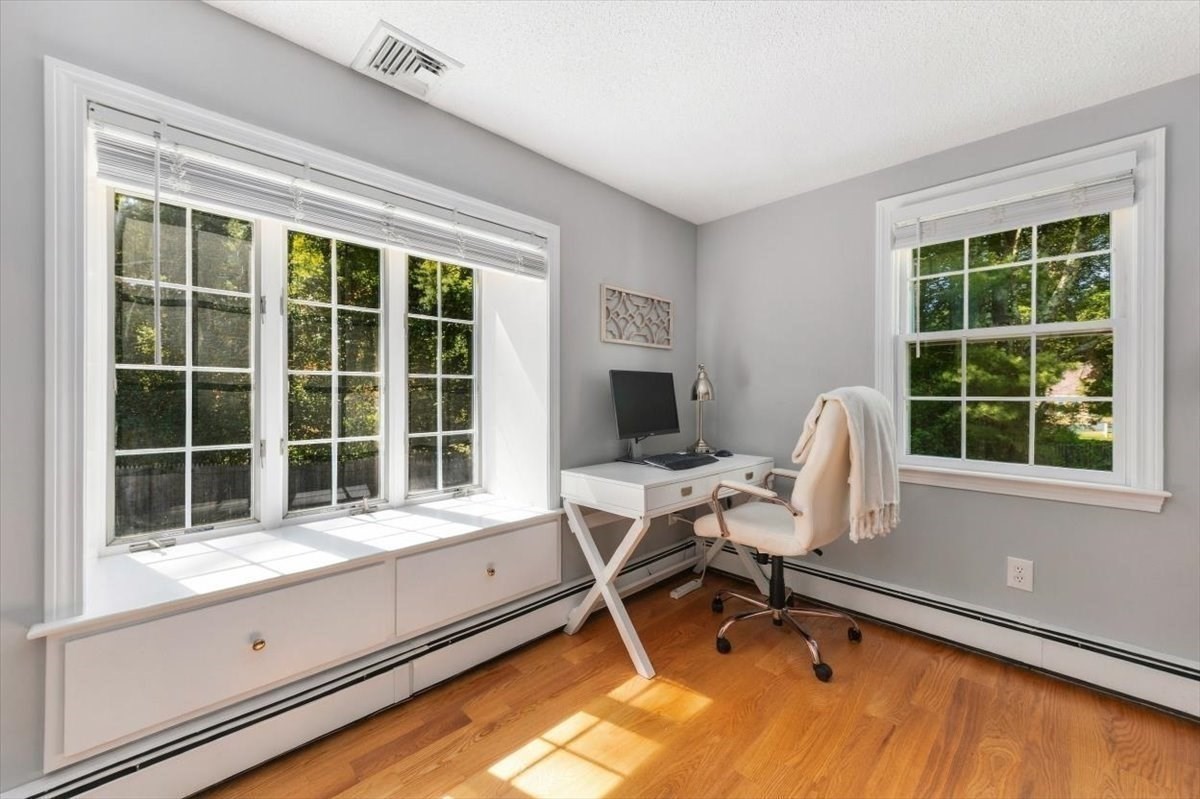 Bright home office with a built-in window seat, large windows, and a white desk.