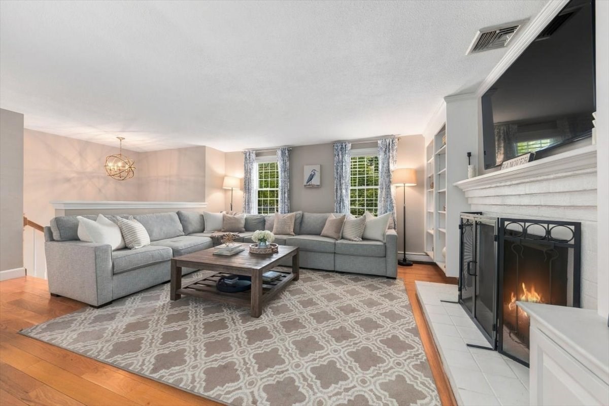 Living room with a gray sectional, patterned rug, and white fireplace with a fire.