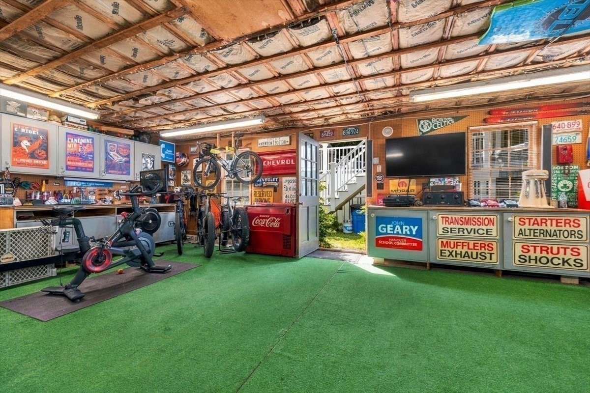 Garage with green turf flooring, exercise equipment, bicycles, and vintage automotive signs.
