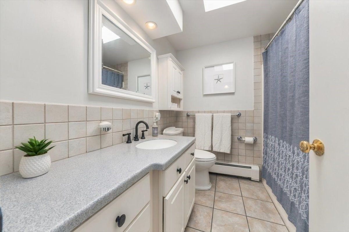 Bathroom with a long white vanity, gray countertop, tiled walls and floor, and blue shower curtain.
