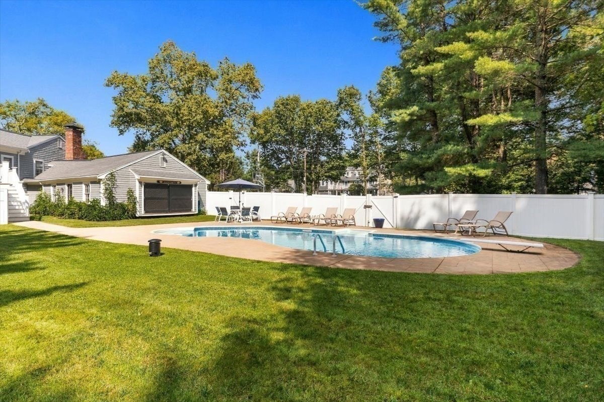 Backyard swimming pool with a paved patio, outdoor chairs, white fence, and detached garage.