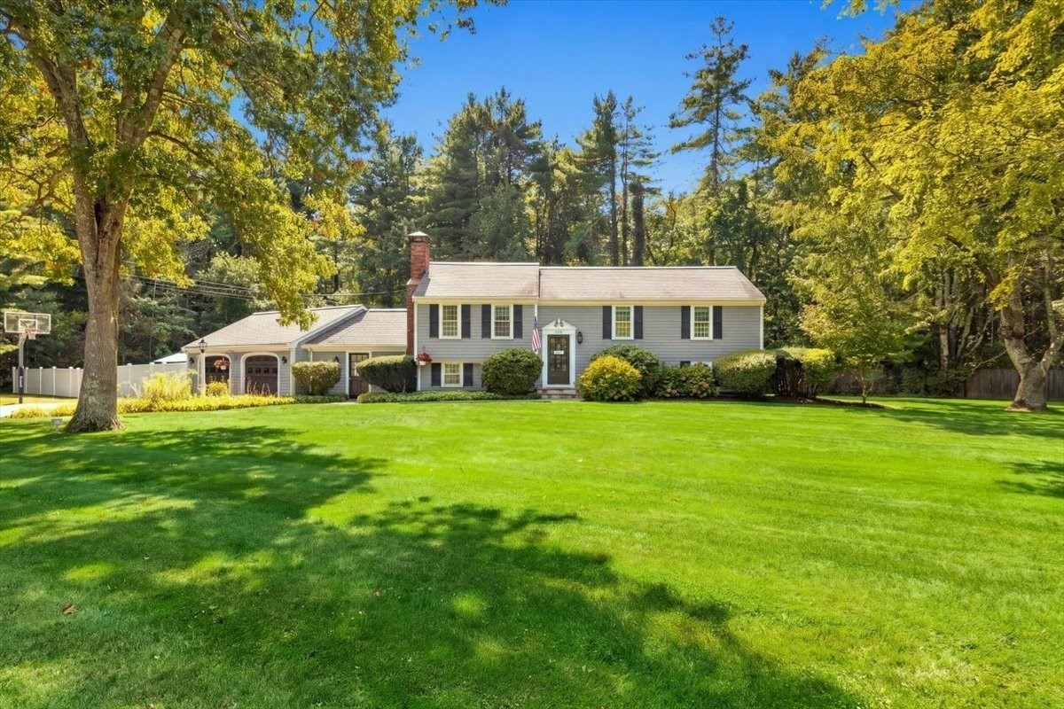 Gray split-level home with attached garage, broad lawn, and mature autumn trees.