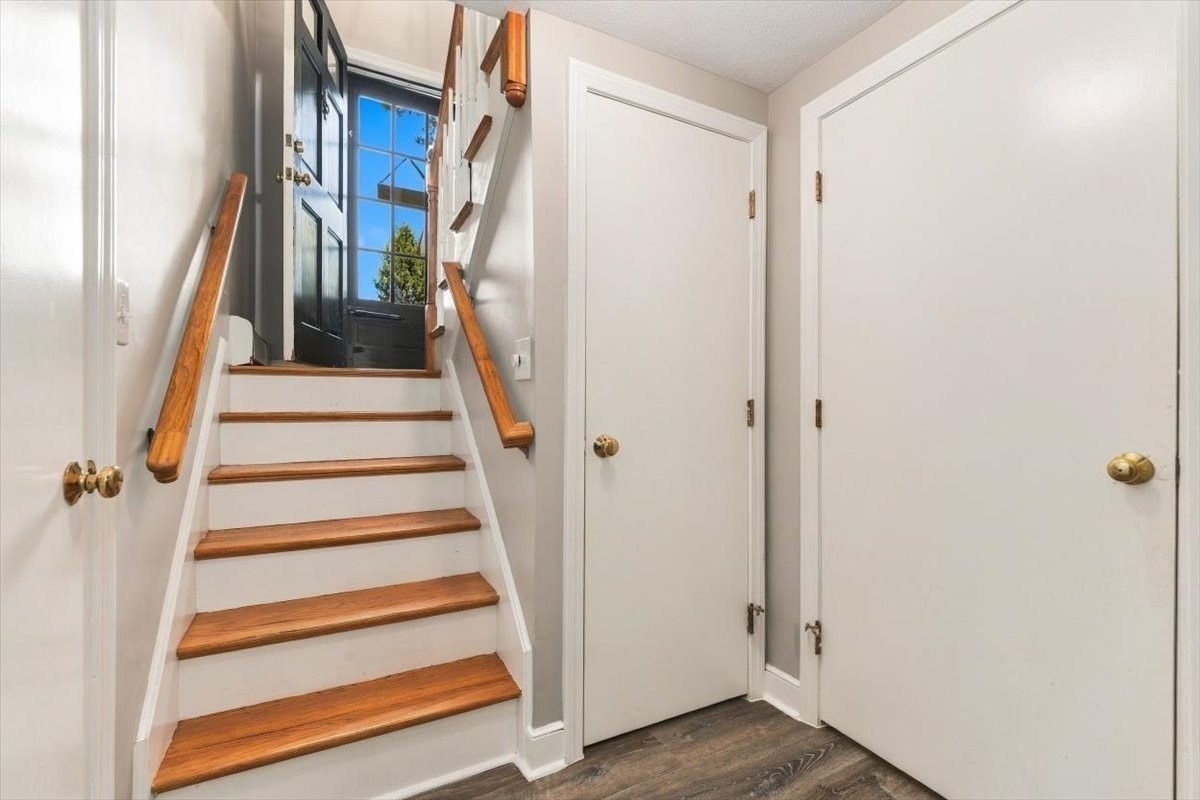 Entry hall staircase with wood treads and handrails leading to a black, windowed front door.