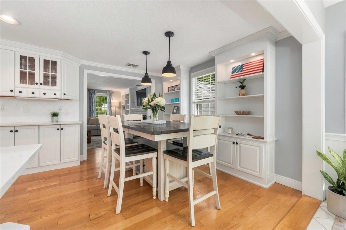 Dining area with a dark-top table, white chairs, hardwood floors, and built-in shelves displaying an American flag.