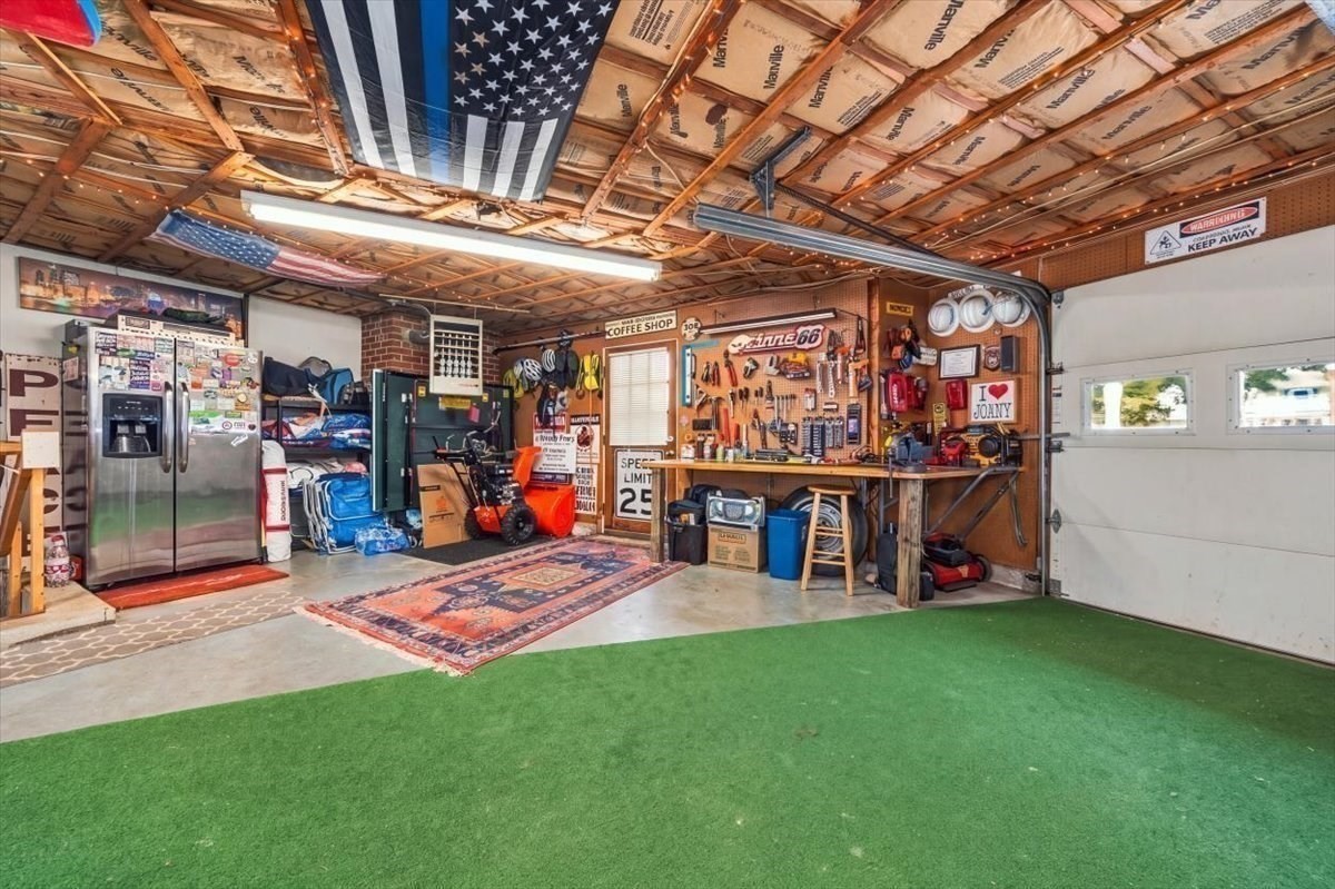 Garage workshop with a tool-covered workbench, American flag ceiling display, and green turf flooring.