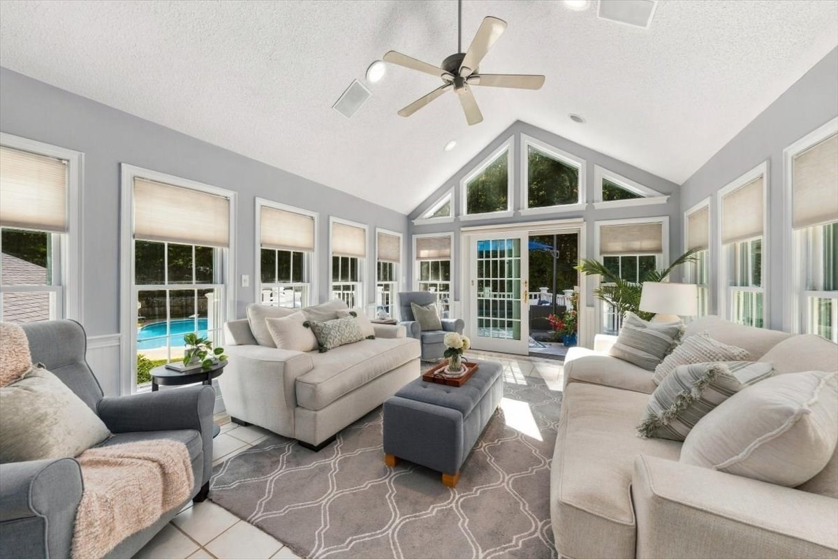 Furnished sunroom with a vaulted ceiling, large windows, and a swimming pool visible outside.