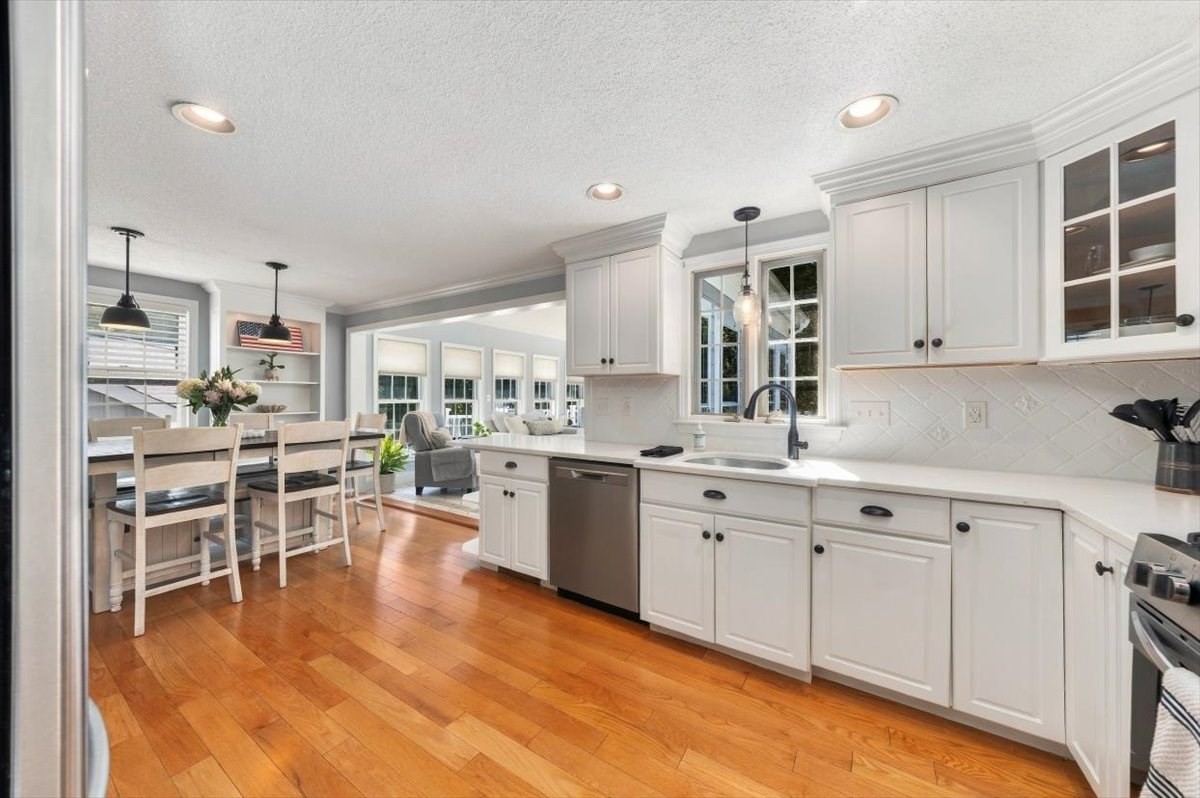 Bright white kitchen with stainless steel appliances, warm hardwood floors, and an adjoining dining area.