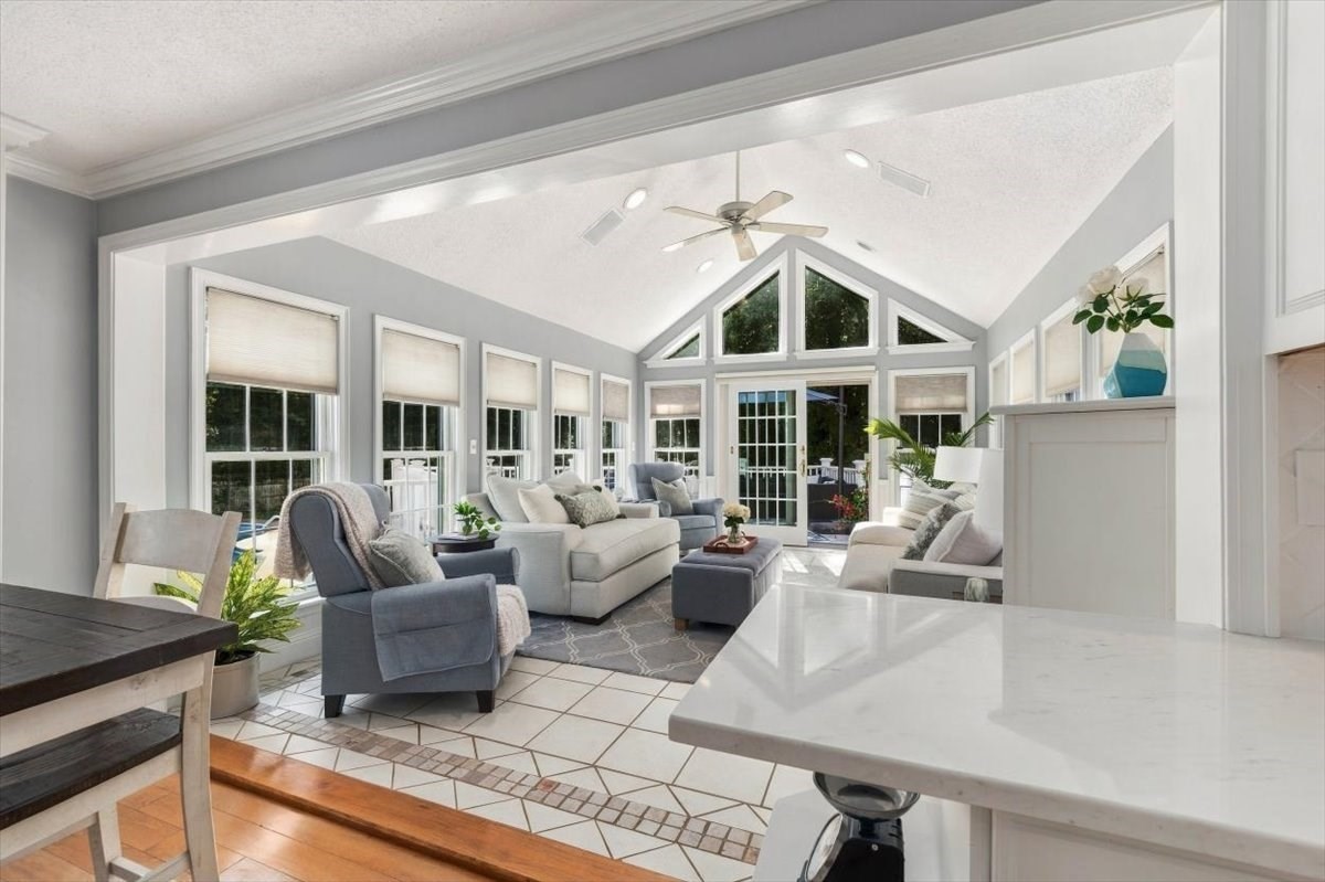 Vaulted sunroom with large windows, gray seating, and a white kitchen island.