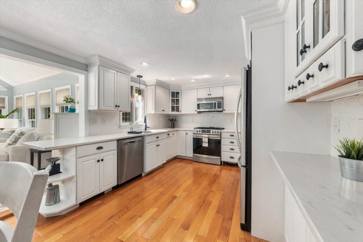 Kitchen with white cabinetry, stainless steel appliances, and warm hardwood floors, opening to a living area.