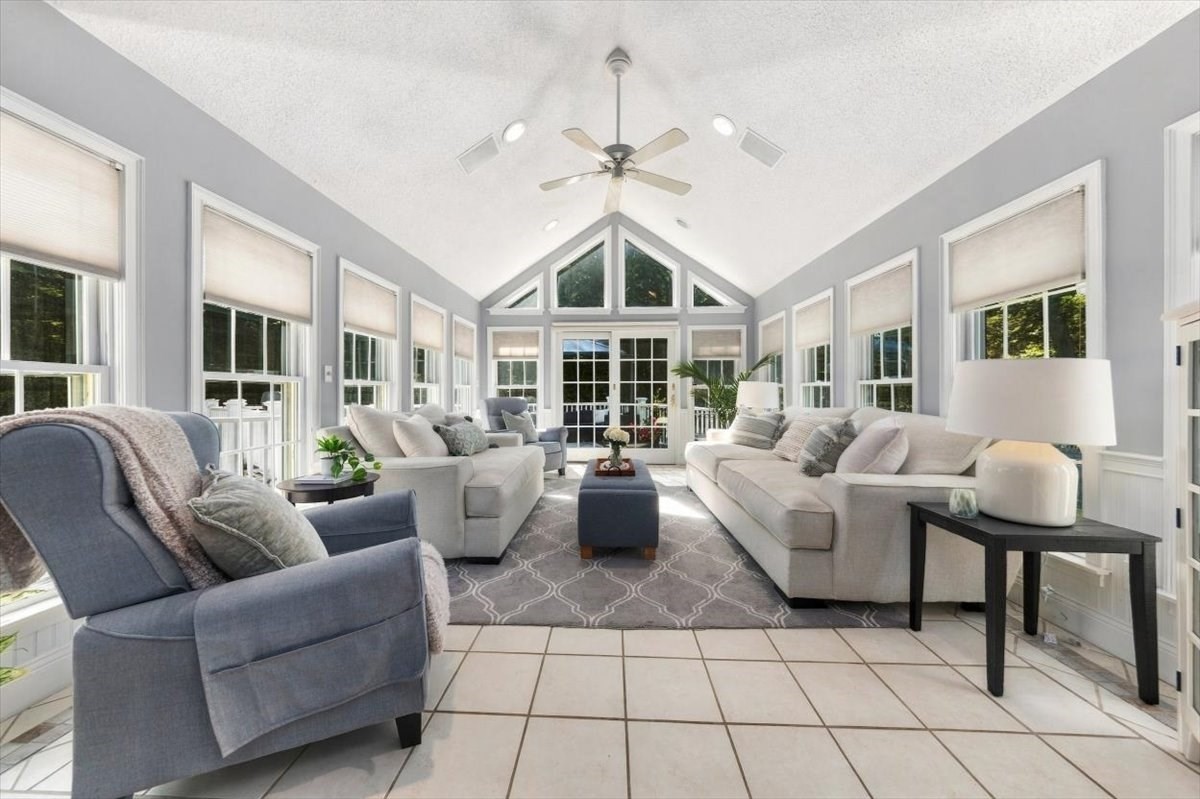 Vaulted living room with large windows, glass doors, and neutral sofas around a patterned rug.