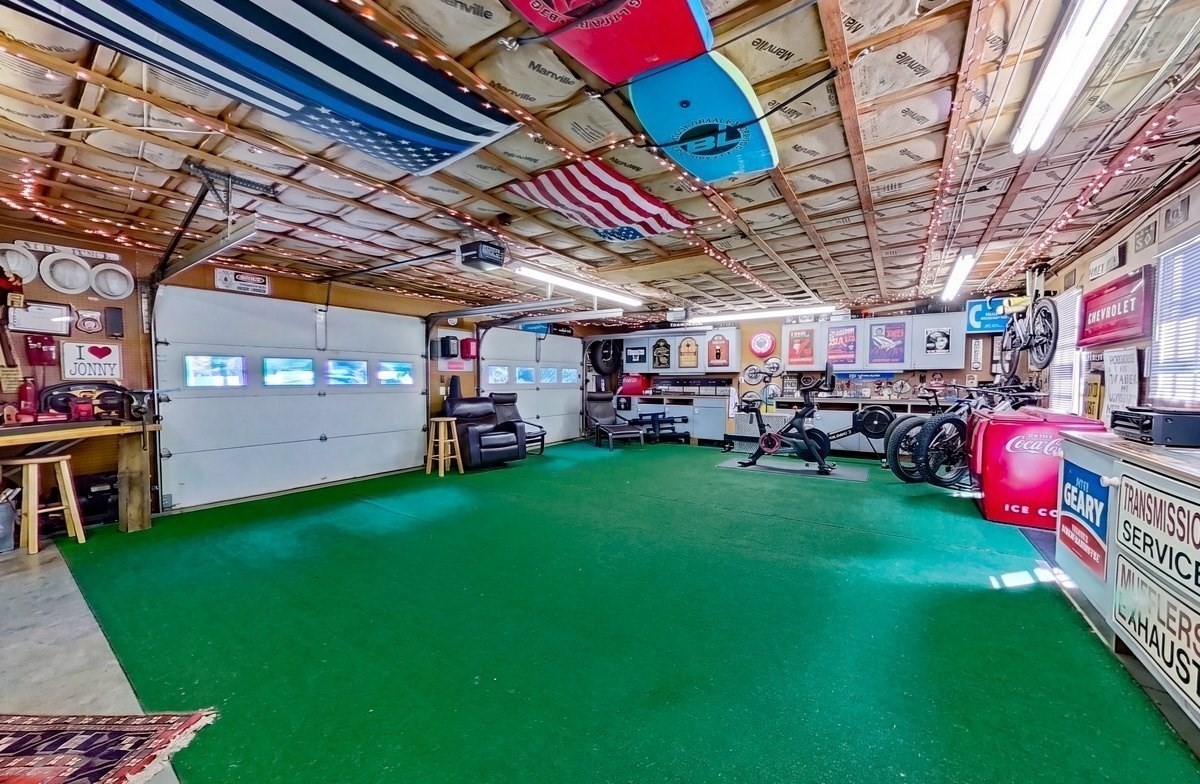 Garage with green carpeting, exercise equipment, bicycles, flags, and vintage memorabilia.